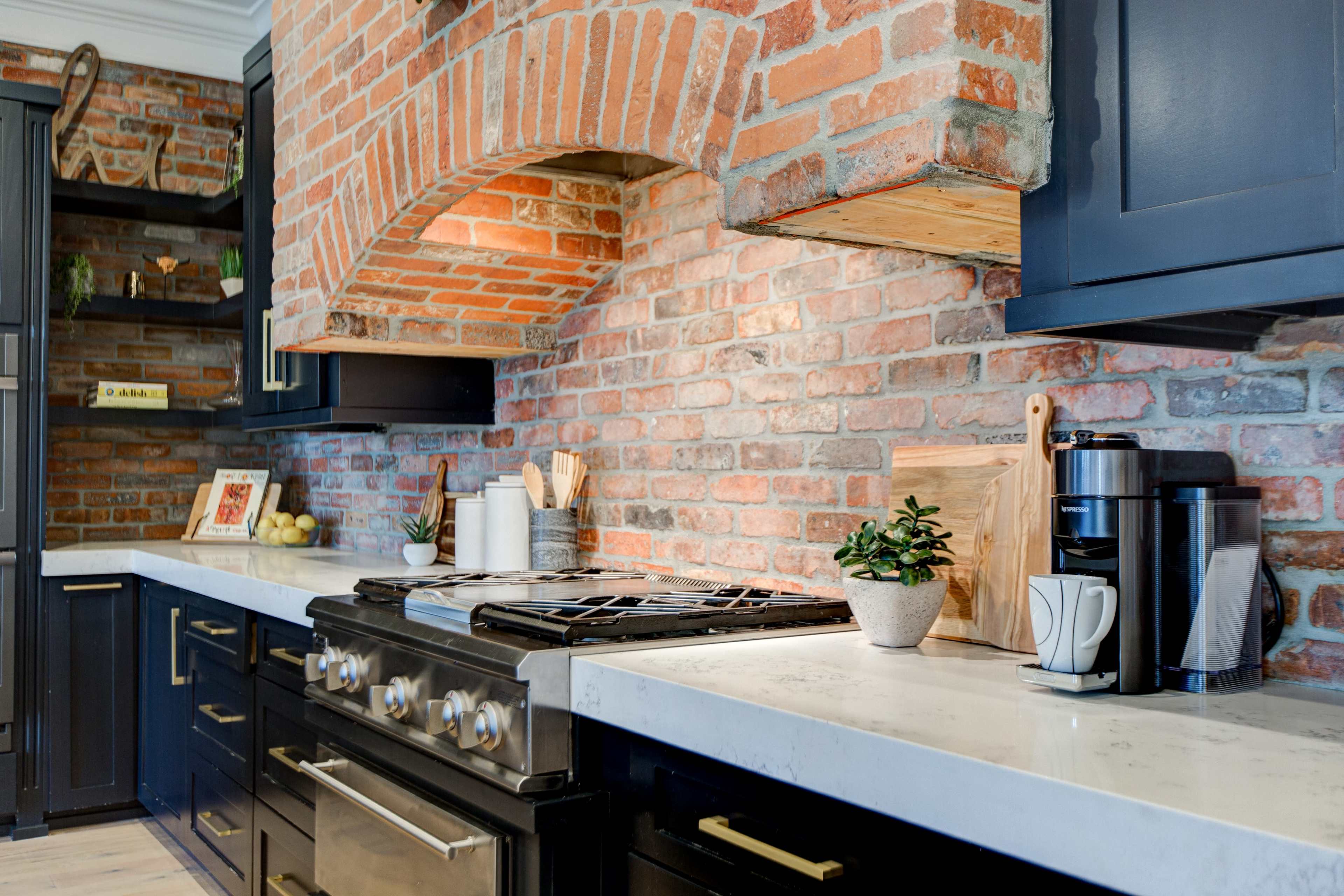 The kitchen features a brick wall backdrop, dark cabinetry, a stainless steel stove, and a countertop with modern appliances and decorative items.