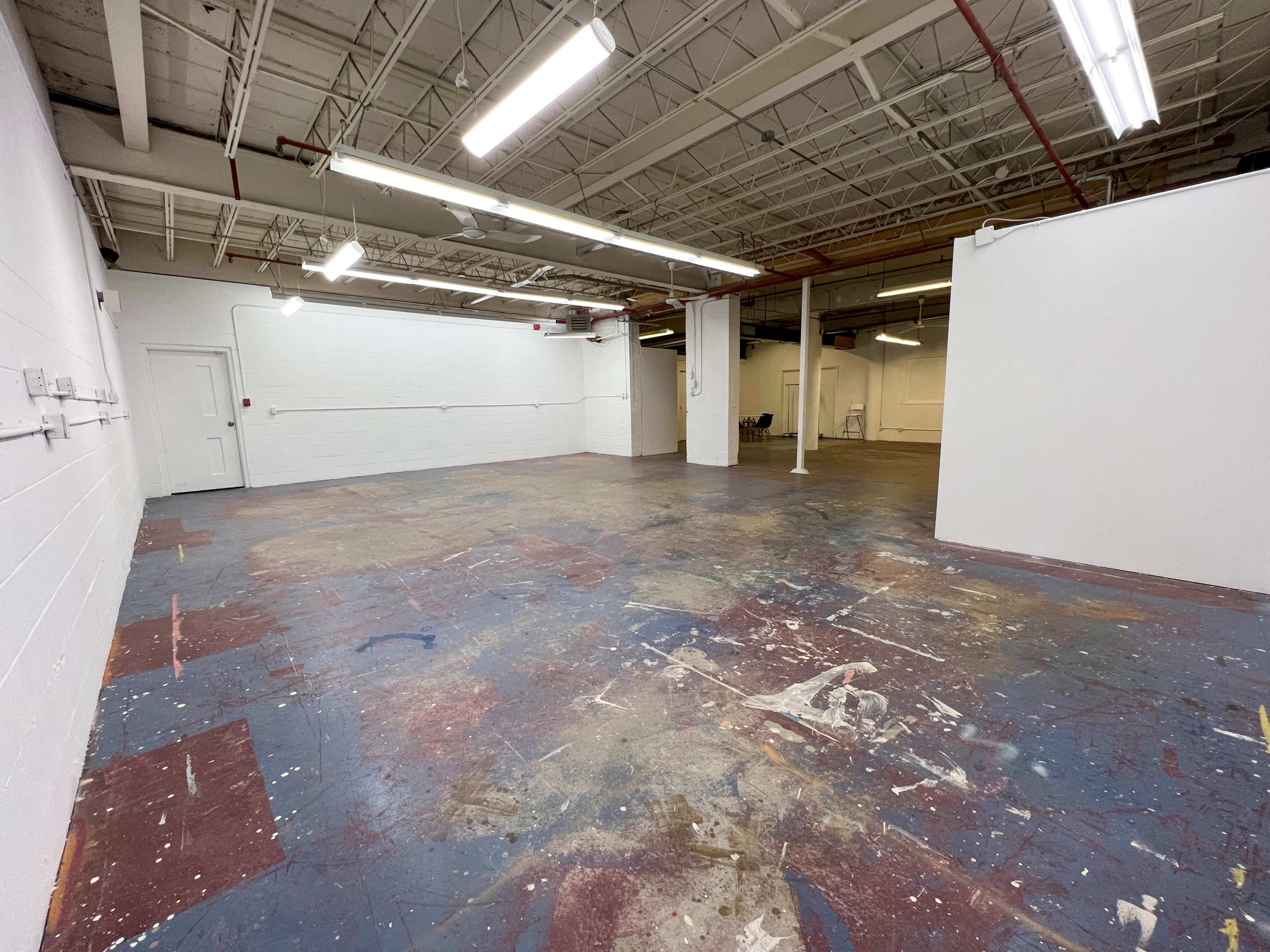 An empty industrial space with a stained concrete floor, white walls, and fluorescent lighting.