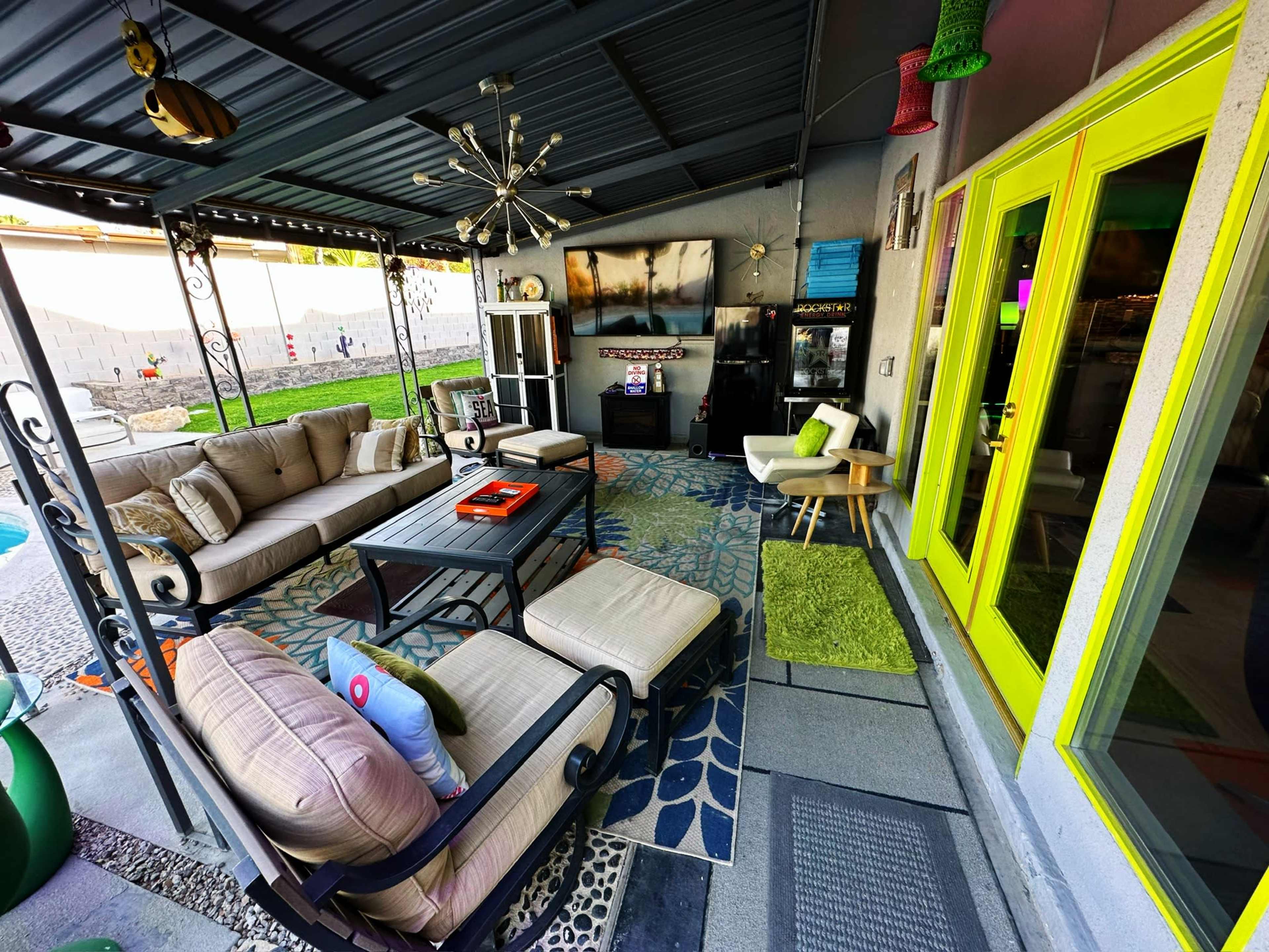 The image shows a patio space furnished with a beige seating arrangement, a black coffee table, and bright green doors.