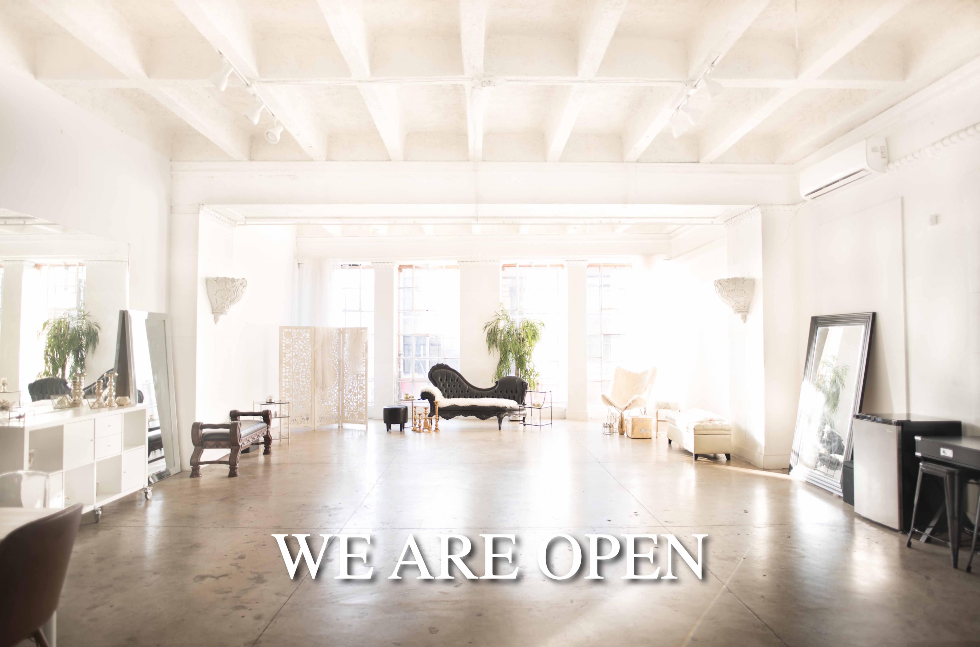 A spacious, bright interior features various seating arrangements and mirrors, with the phrase "WE ARE OPEN" prominently displayed.