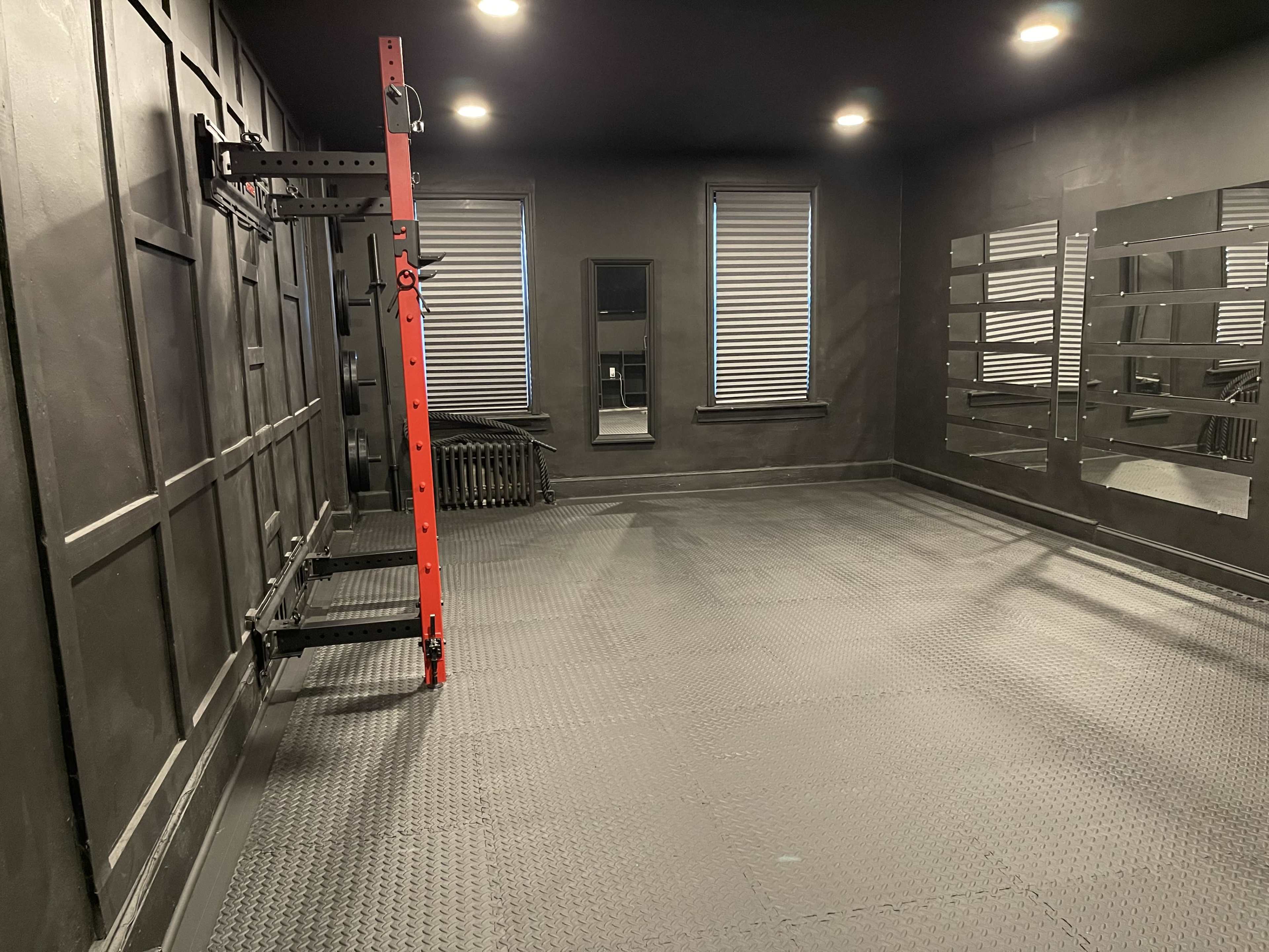 An empty room with black walls and flooring, featuring a red rack on one side and mirrors on the opposite wall.