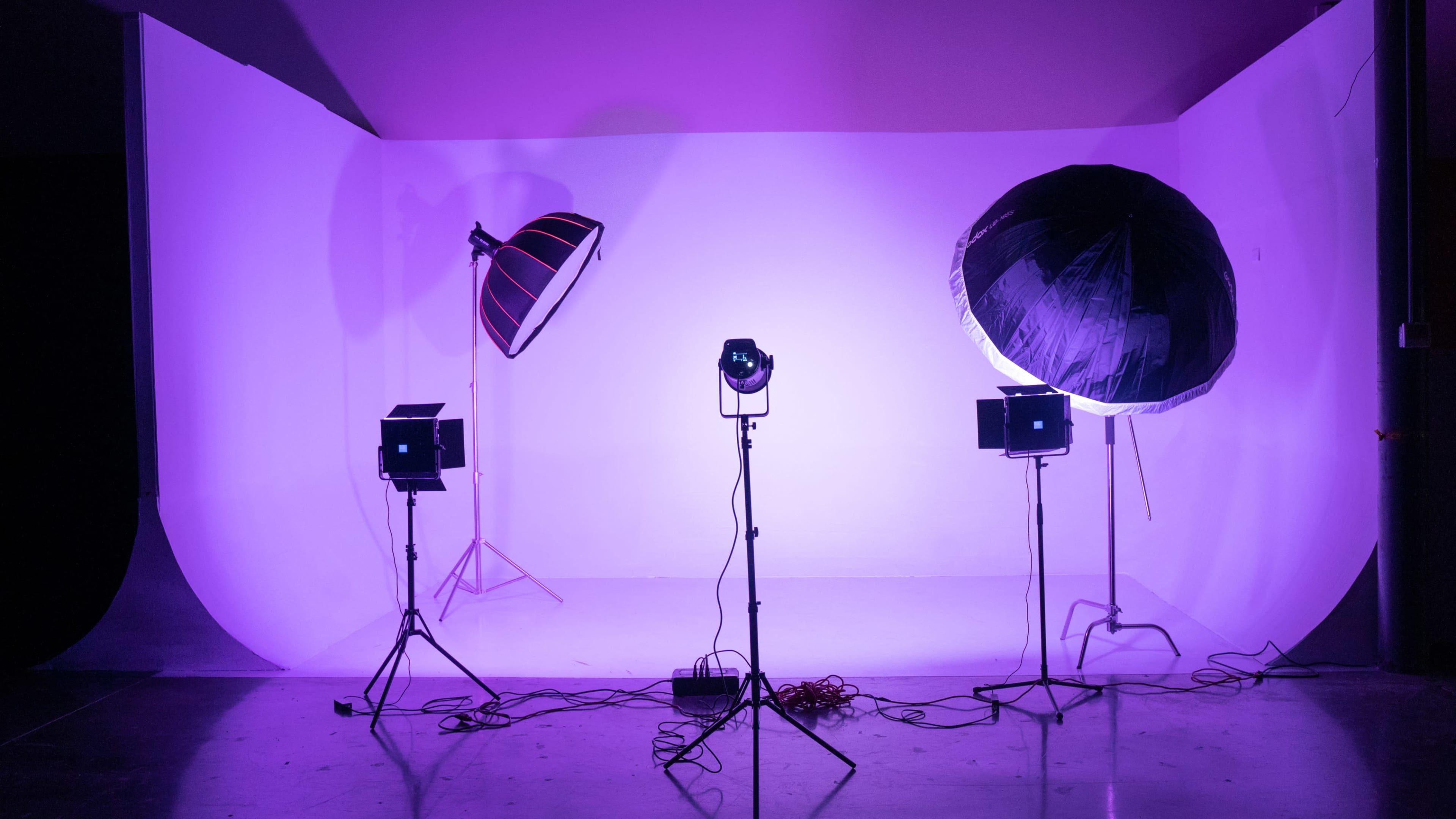 A photography studio setup features two large lights and three smaller lights positioned around a purple backdrop.