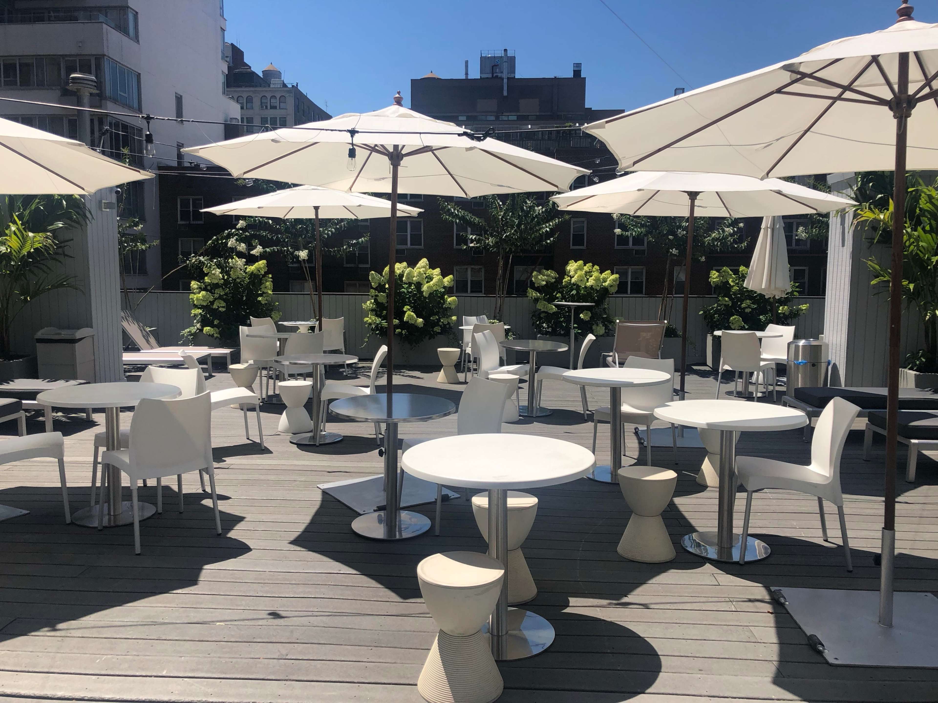 An outdoor seating area with white tables, chairs, and umbrellas arranged on a wooden deck.