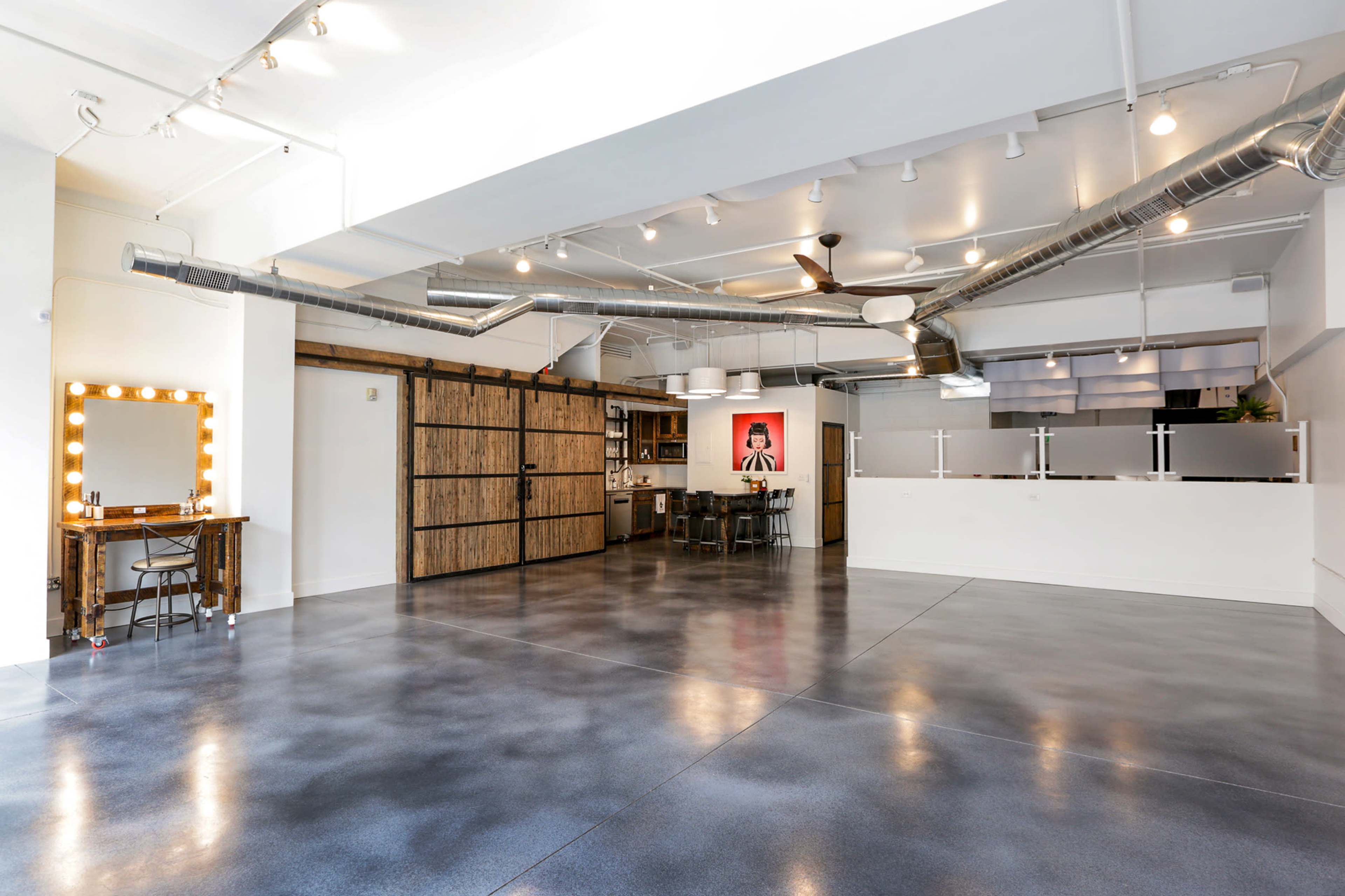 An open, modern studio space with polished concrete floors, exposed ductwork, and a kitchenette area featuring a sliding barn door.