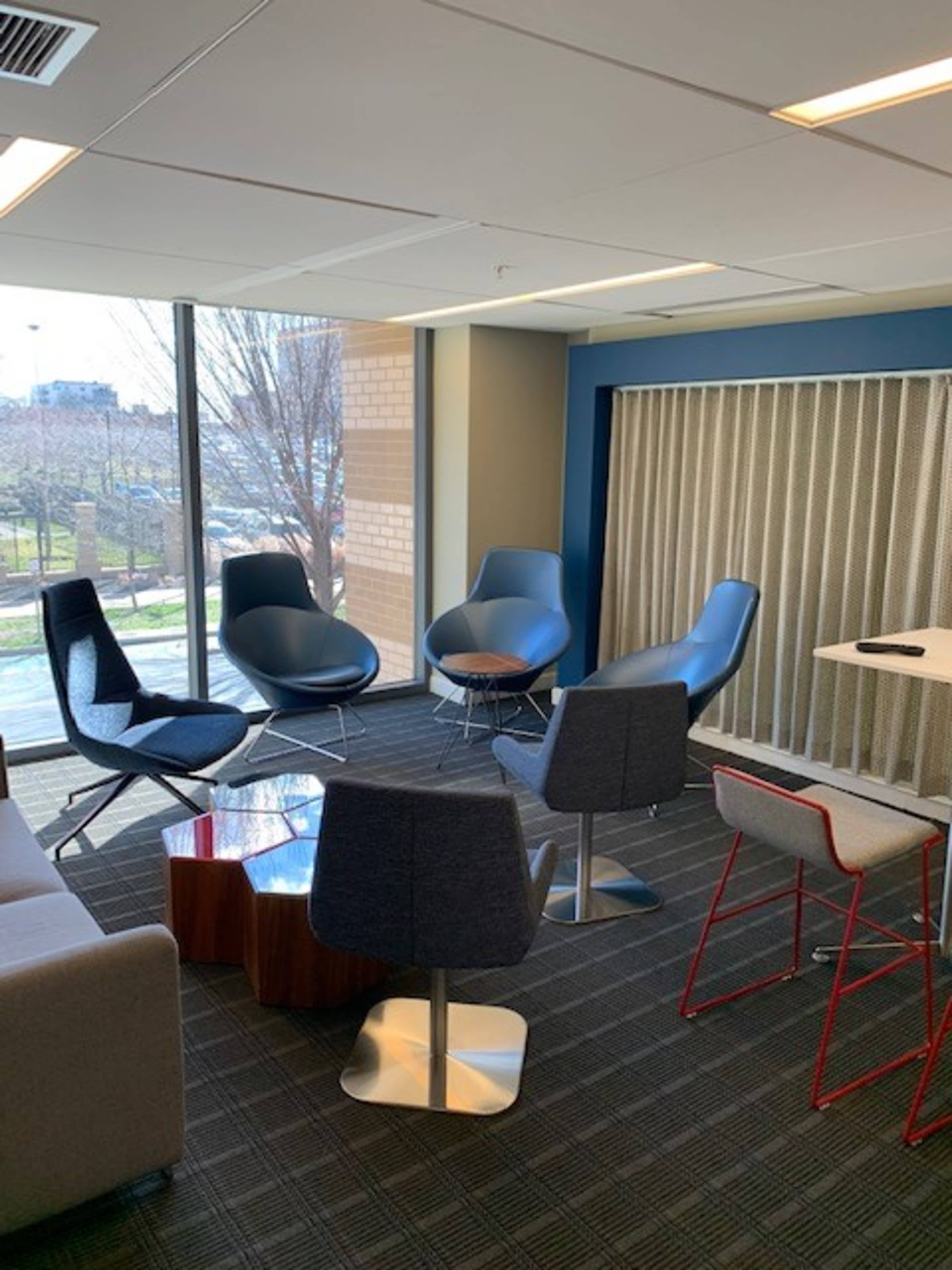 A modern office space with several stylish chairs arranged around a small table near large windows.