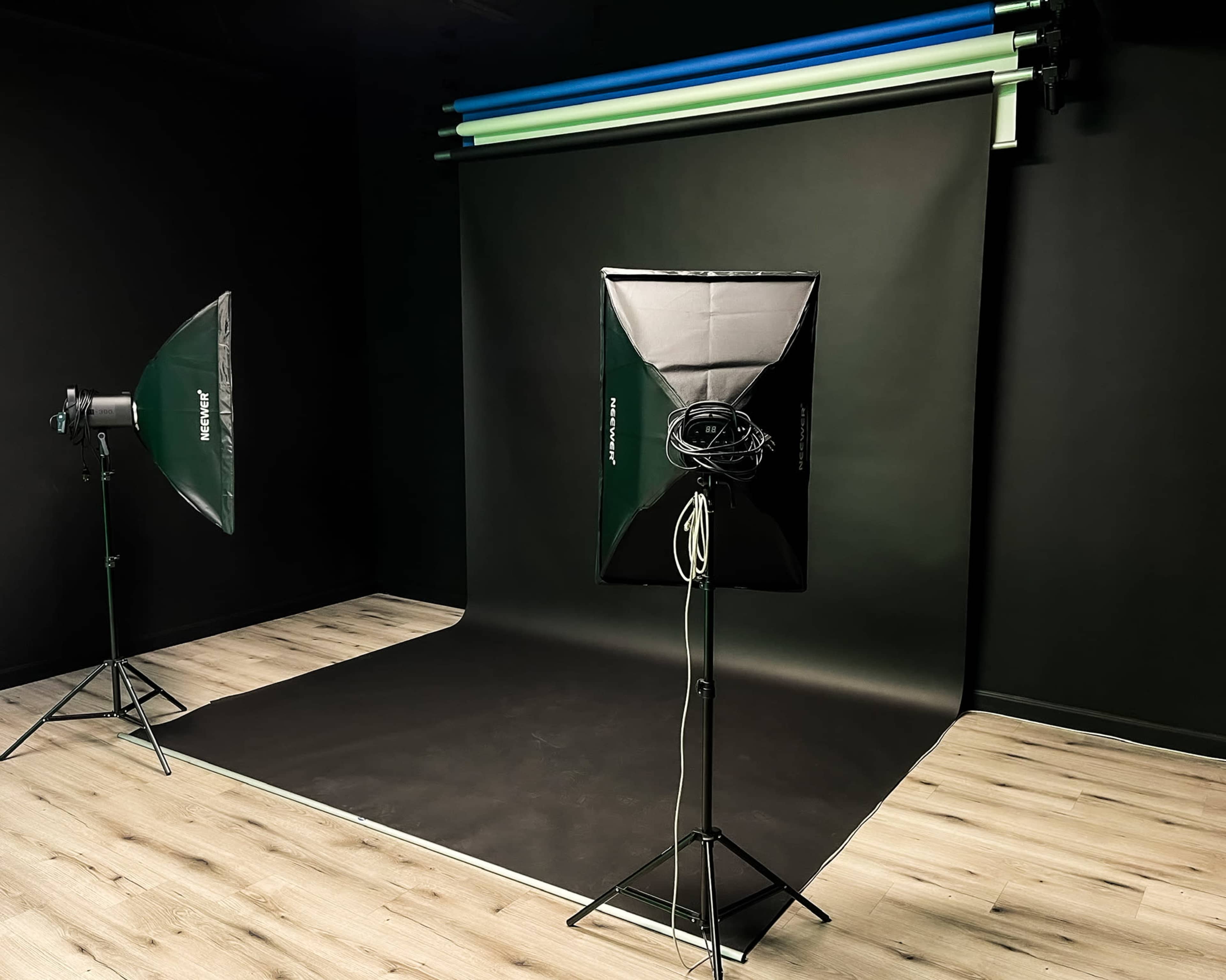 A photo studio setup featuring a black backdrop, softbox lights, and a wooden floor.