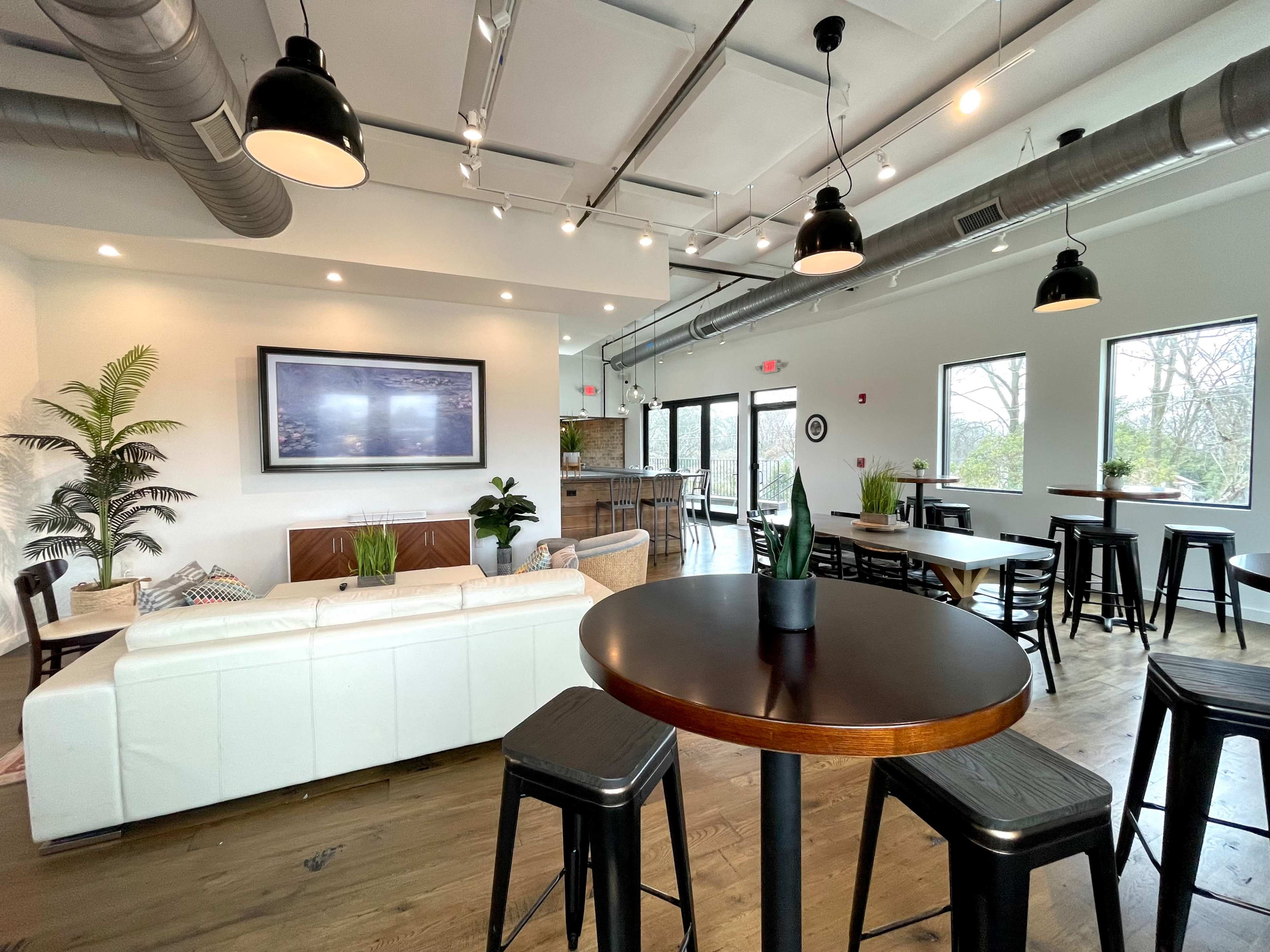 A modern, open lounge area with a white sectional sofa, black metal tables, and large windows letting in natural light.