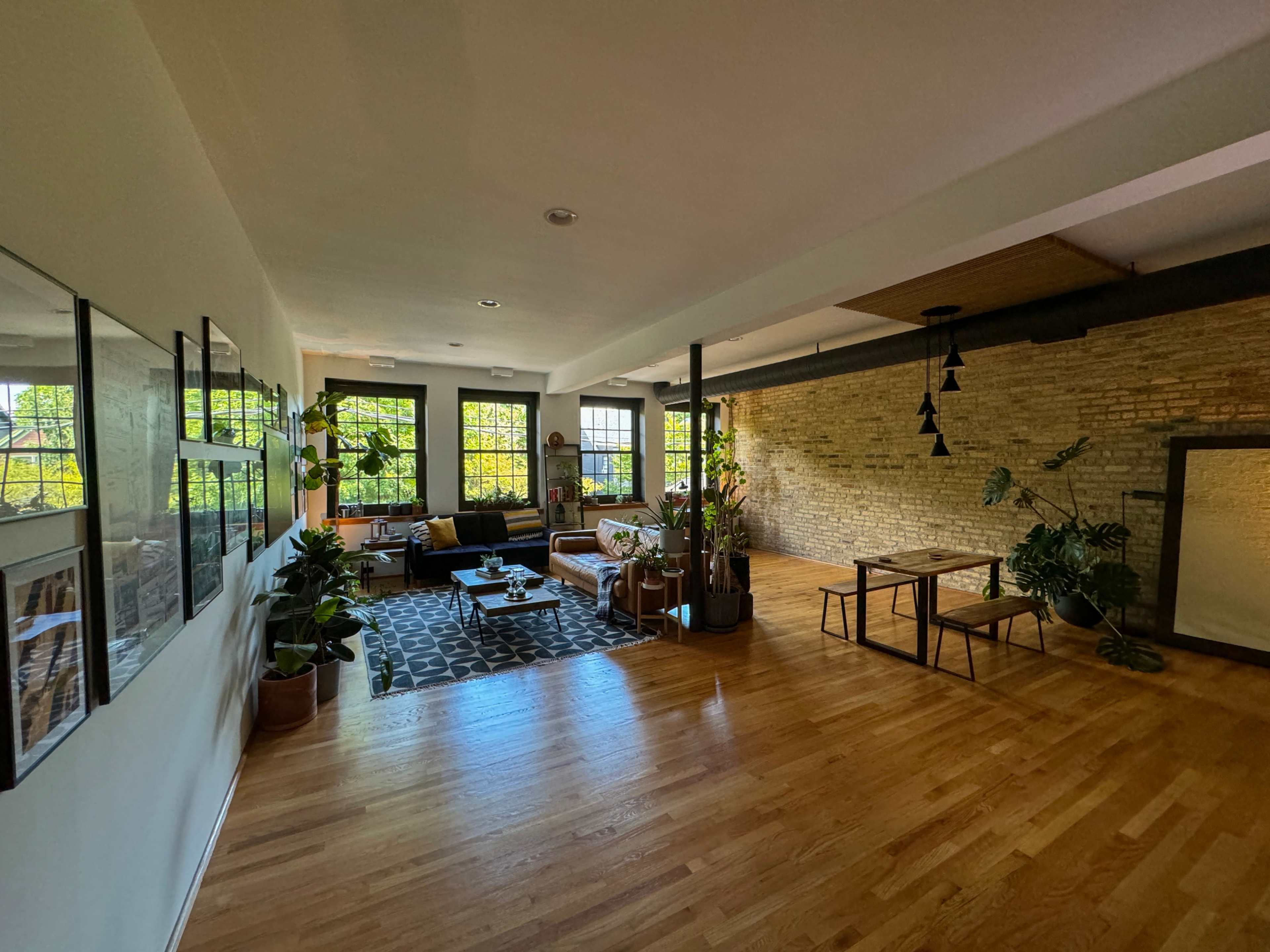 A spacious living area features a combination of wooden flooring, large windows, and a mix of modern and plant elements.