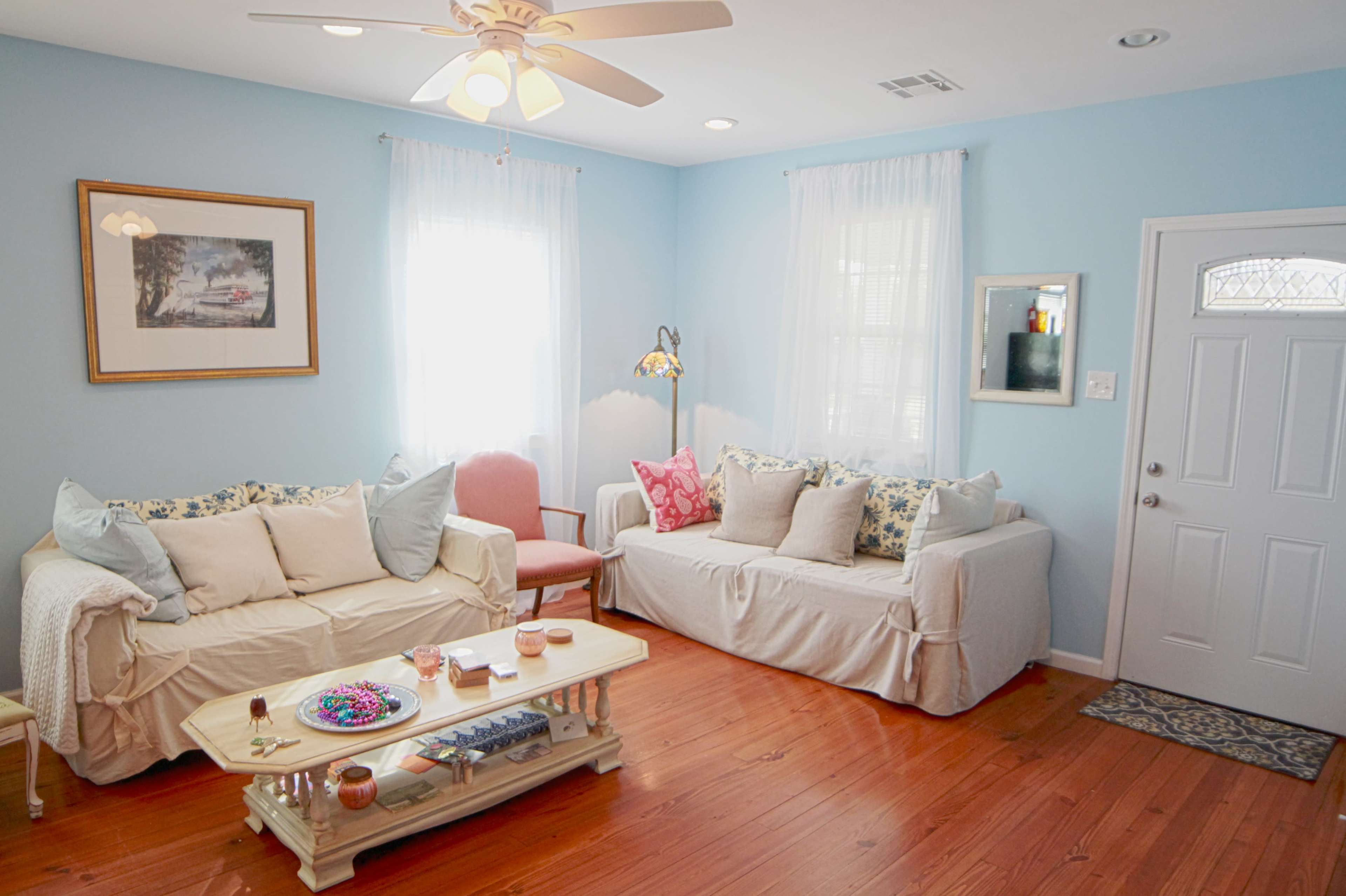 The image shows a light blue living room with two sofas, a coffee table, and a door leading outside.