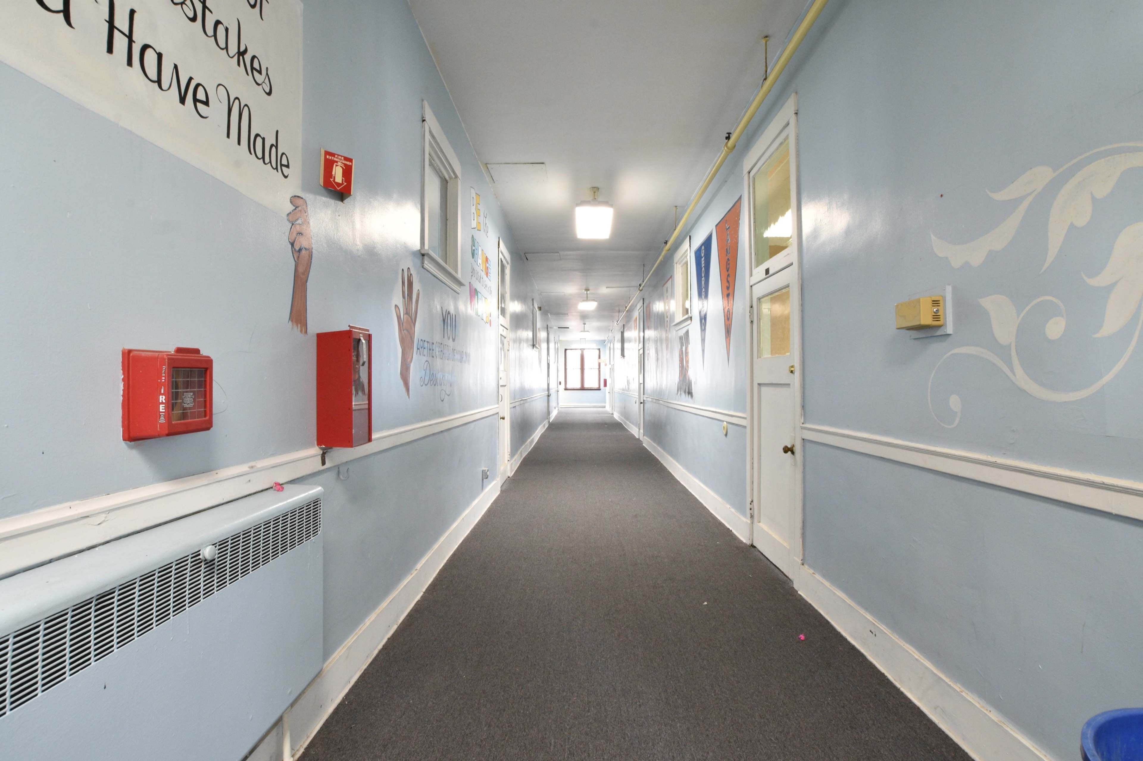 A long hallway with blue walls, a carpeted floor, and several doors along the sides.
