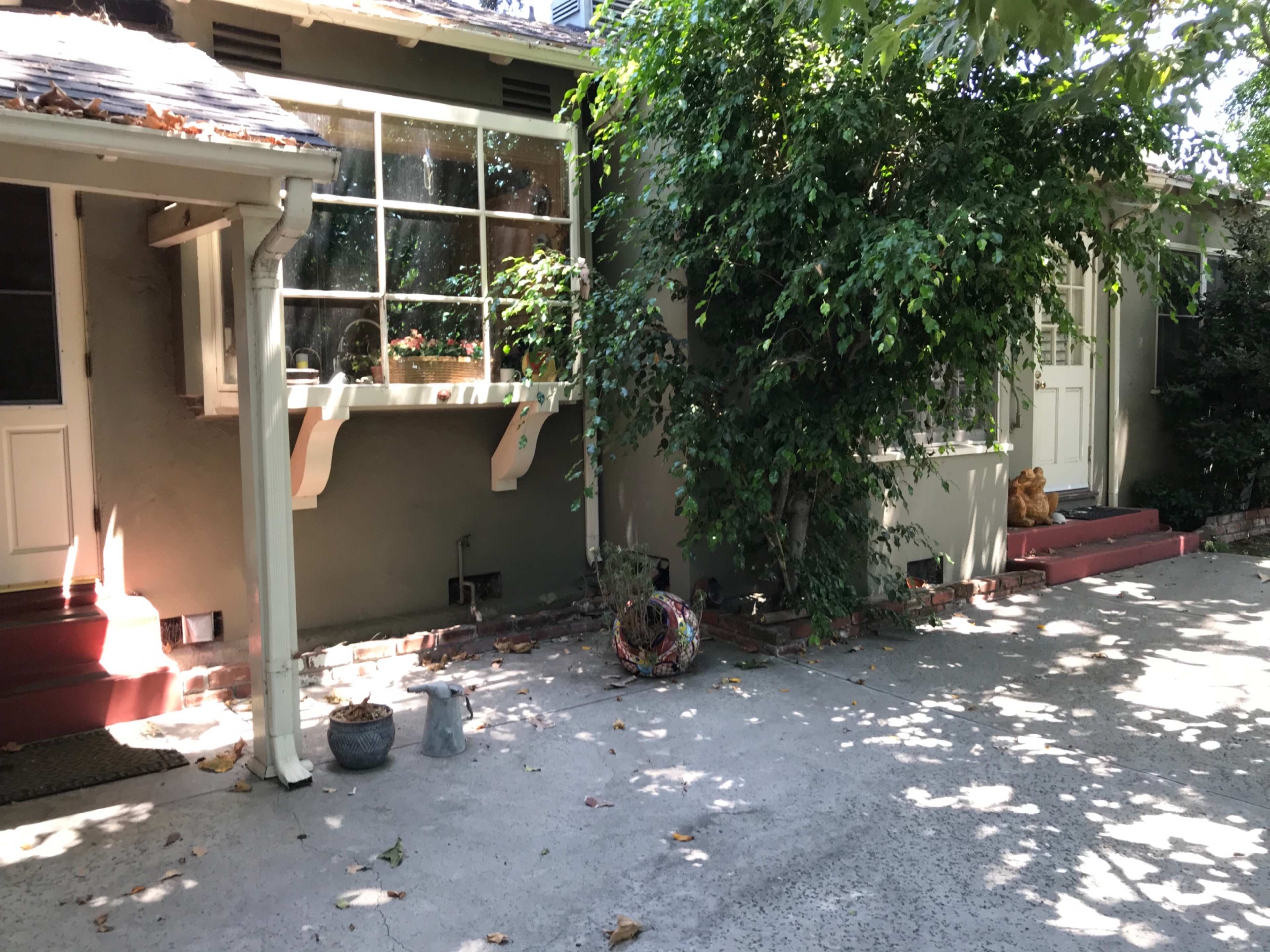 The scene shows a residential area with a patio bordered by a bush, two entrances, and a few decorative elements on the ground.