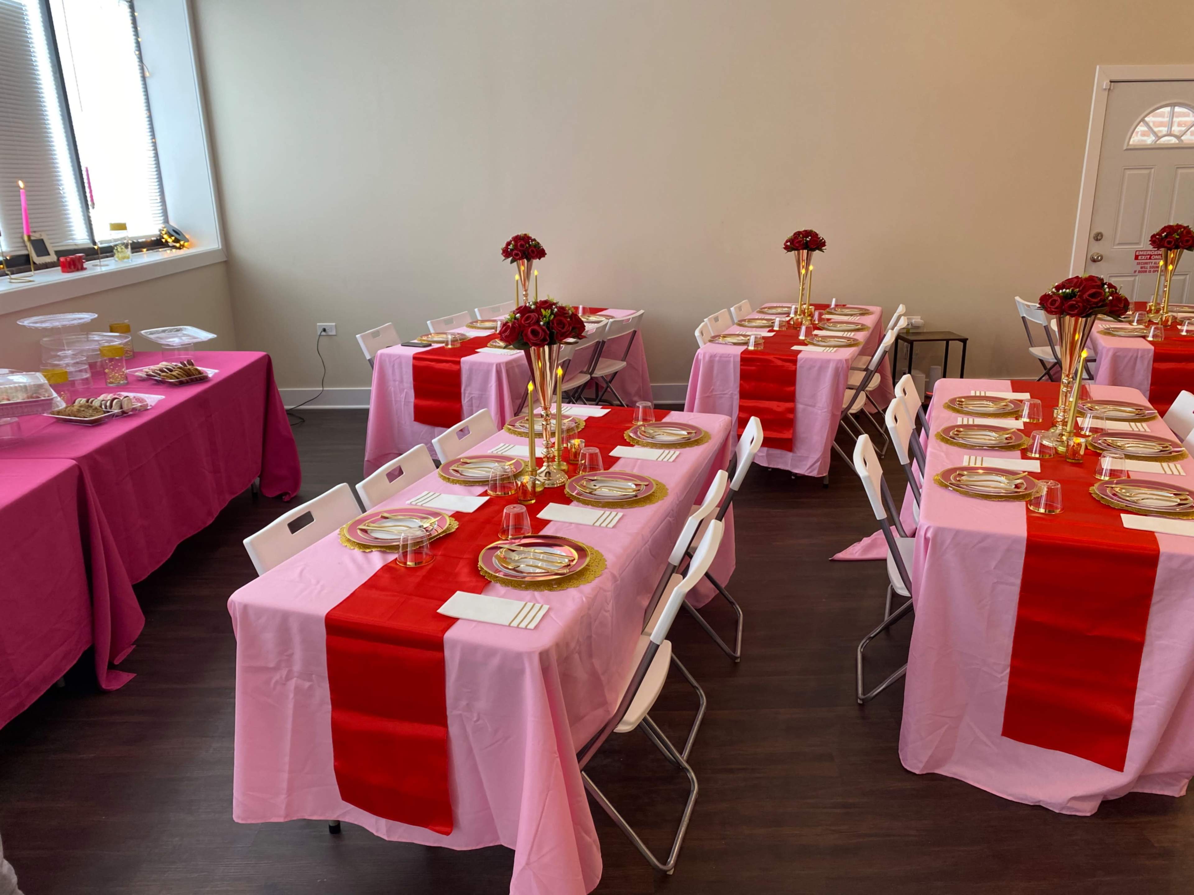 The room features several tables set with pink and red tablecloths, gold dinnerware, and floral centerpieces arranged in vases.