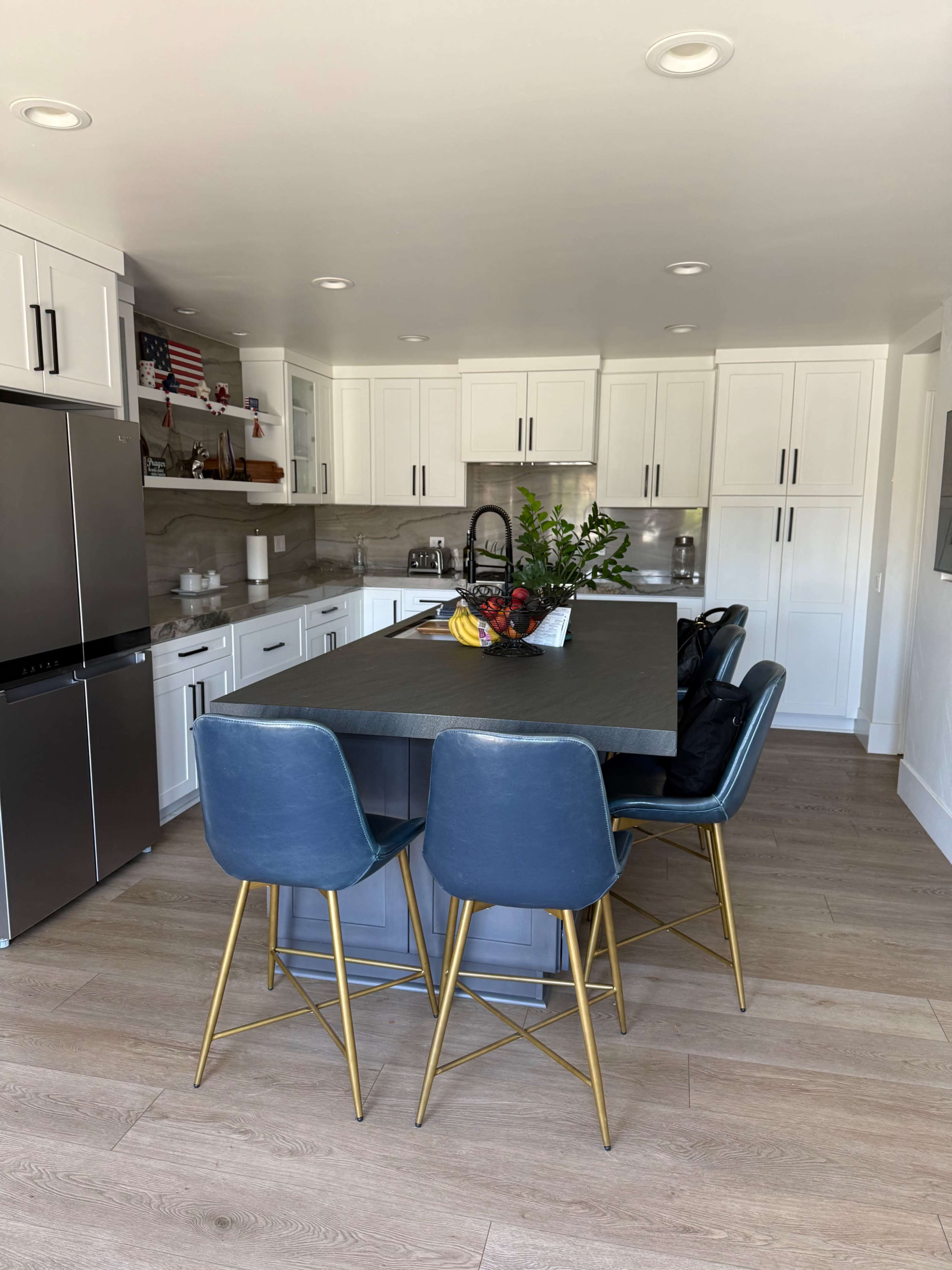 A modern kitchen features a large island with seating, white cabinetry, and stainless steel appliances.
