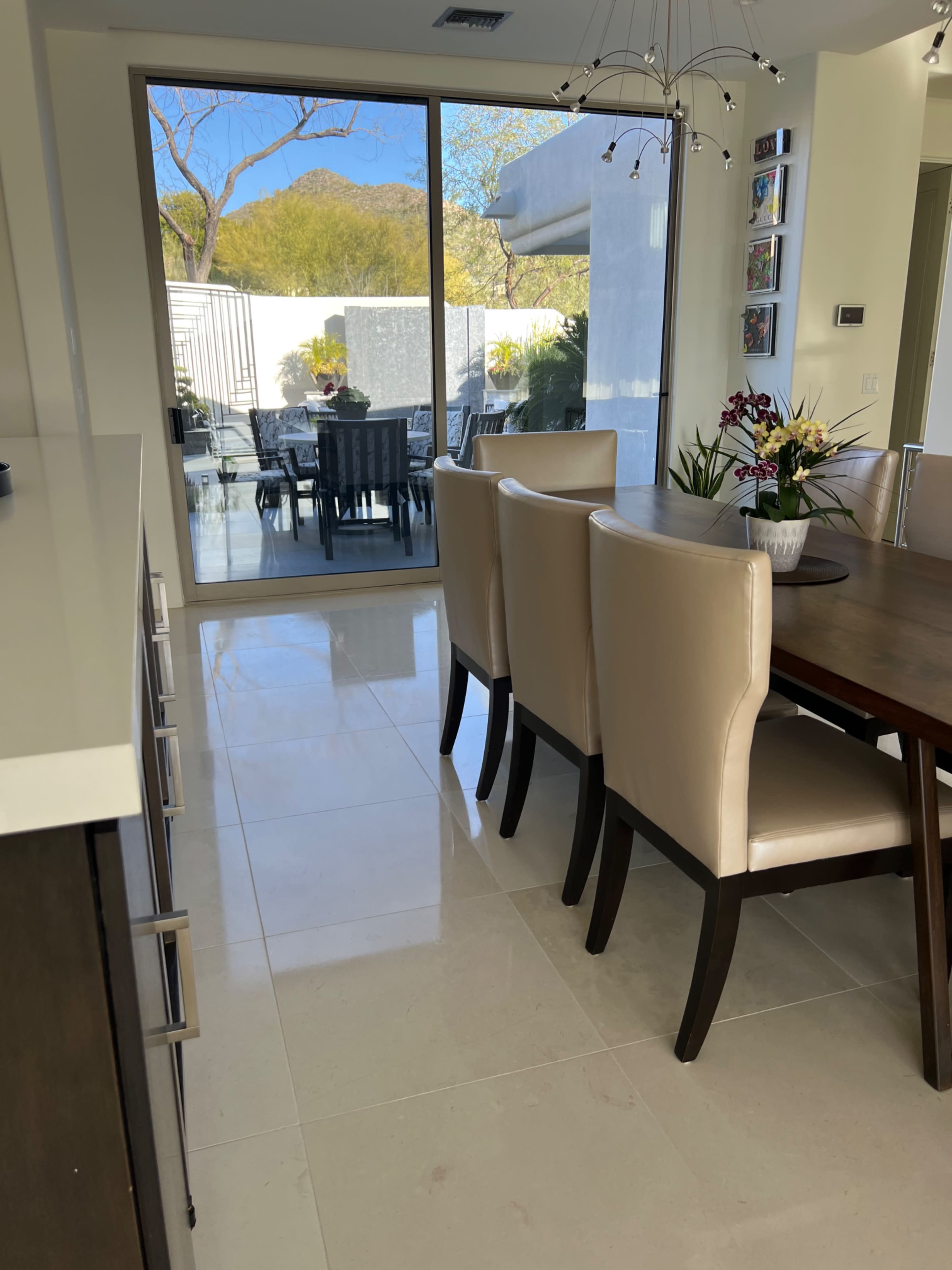 A dining area with a large table and beige chairs is visible through a glass sliding door that leads to an outdoor space with seating and plants.