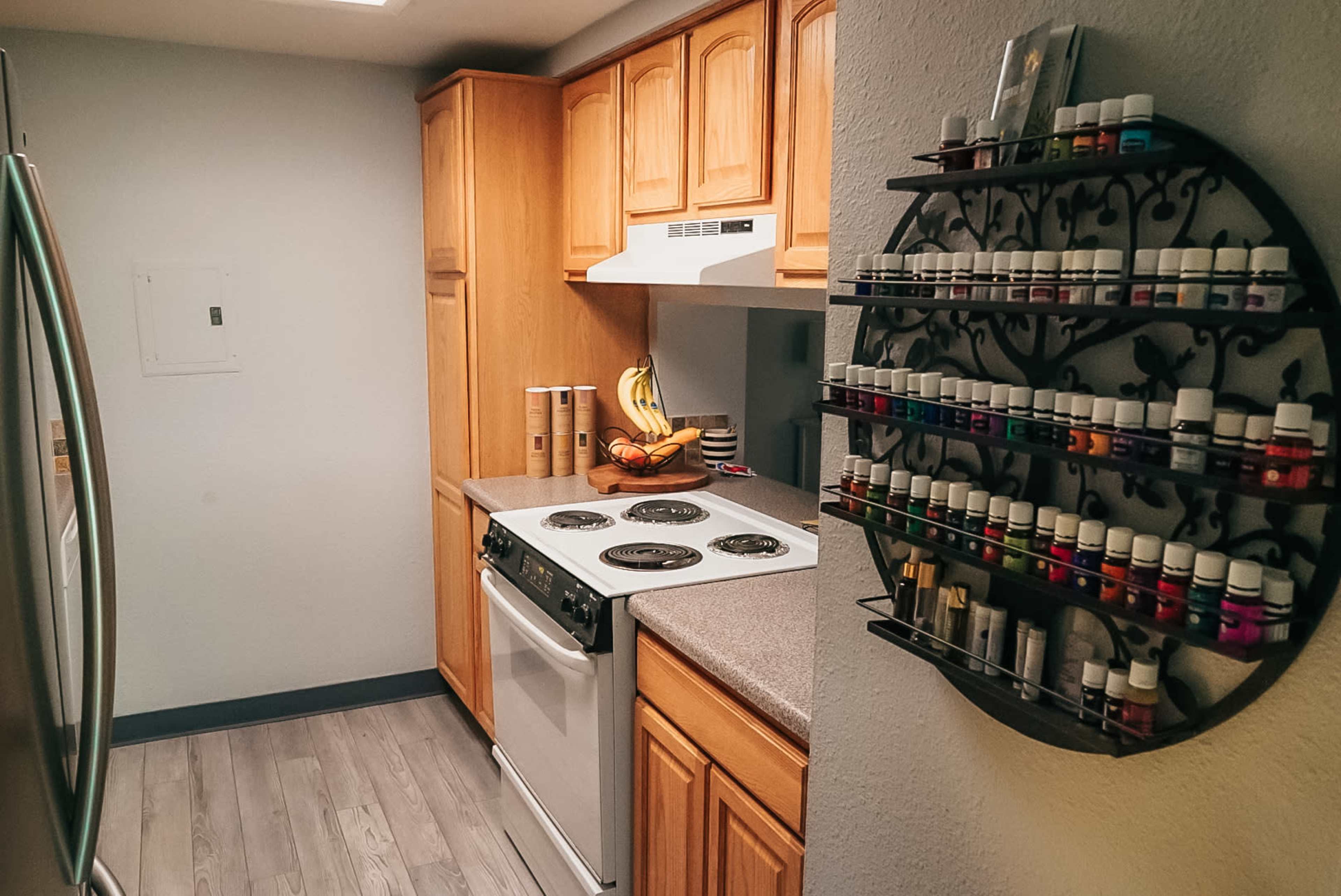 A compact kitchen features wooden cabinetry, a stove, and a wall-mounted rack displaying various essential oils.
