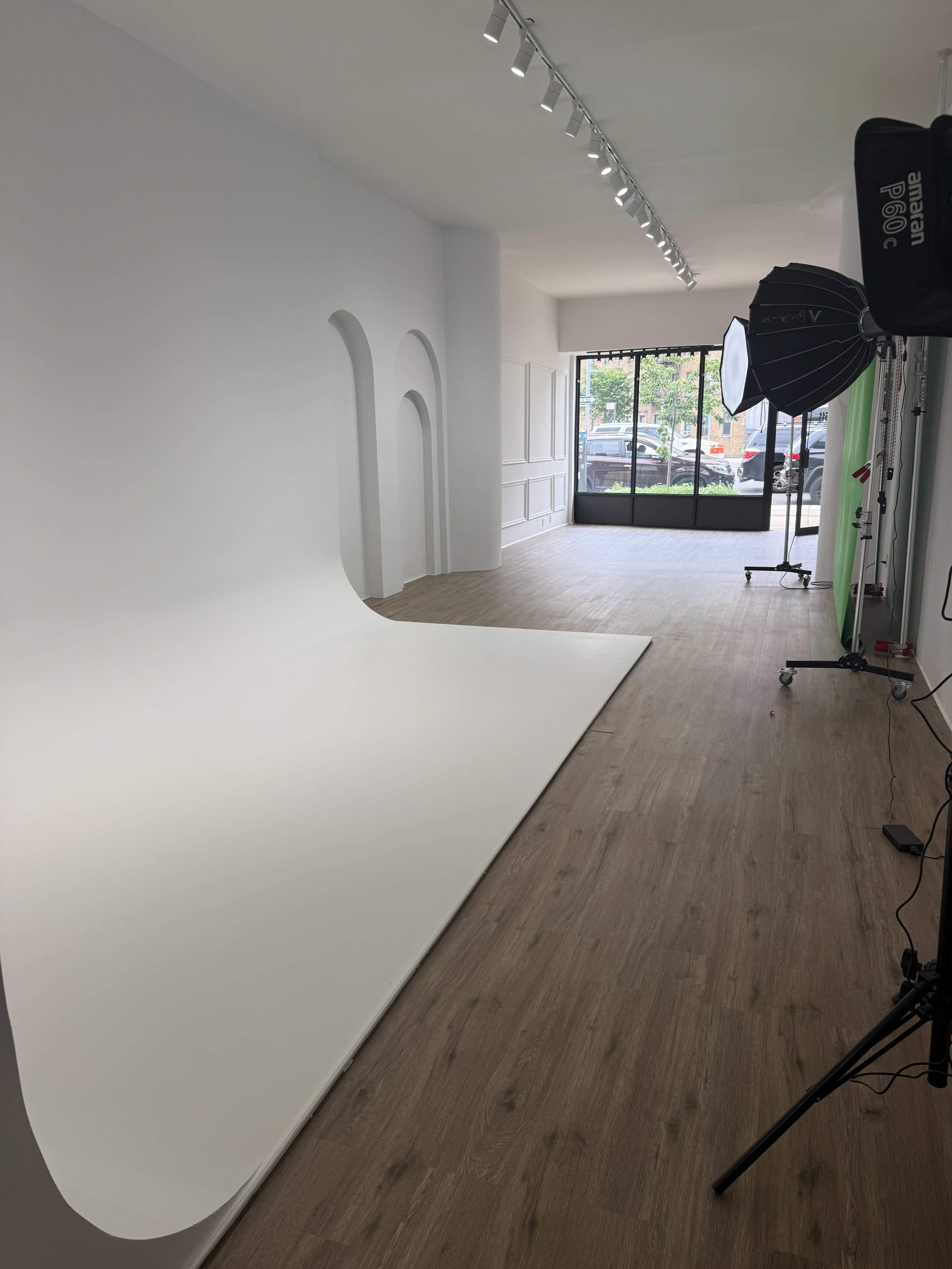 The image shows a photography studio with a white backdrop, wooden flooring, and various lighting equipment arranged along one side.