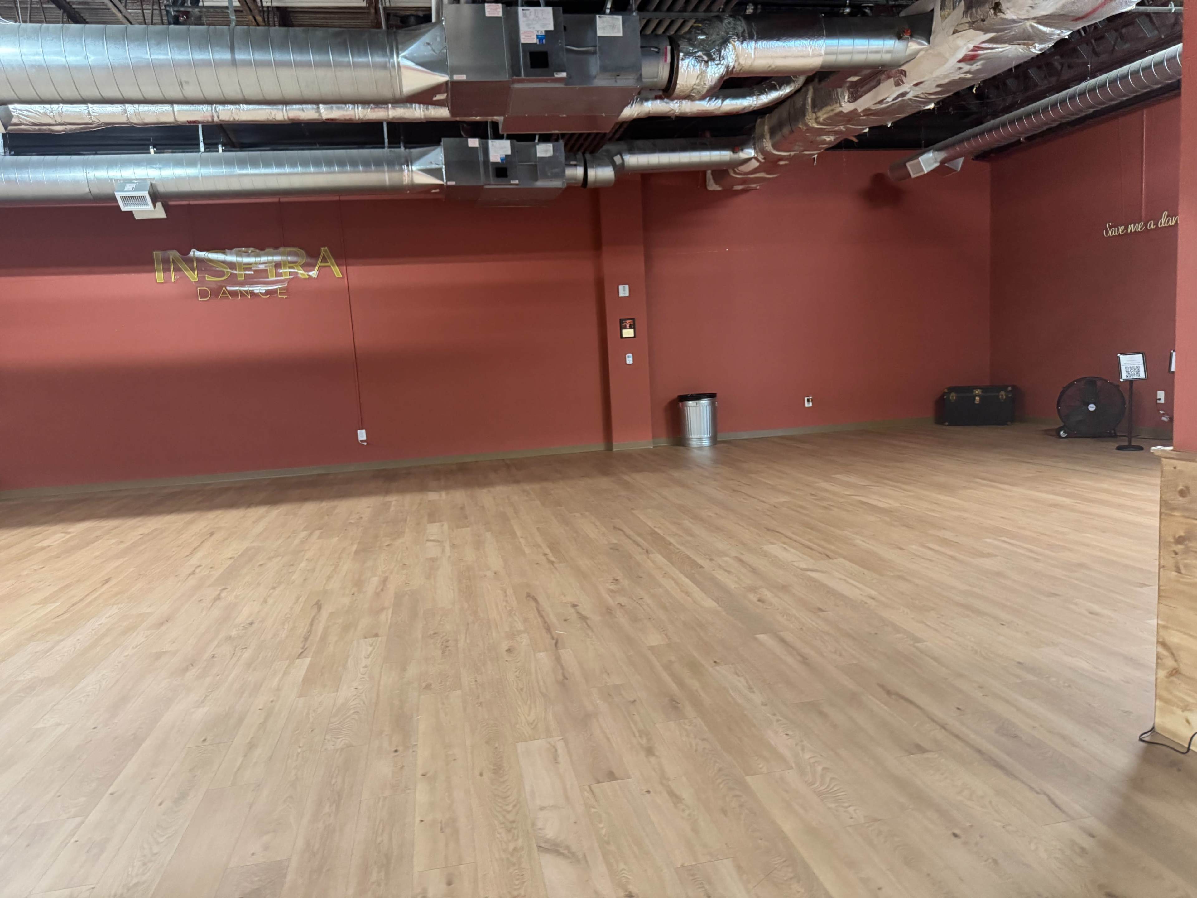 The image shows an empty studio space with wooden flooring and exposed ductwork on the ceiling.
