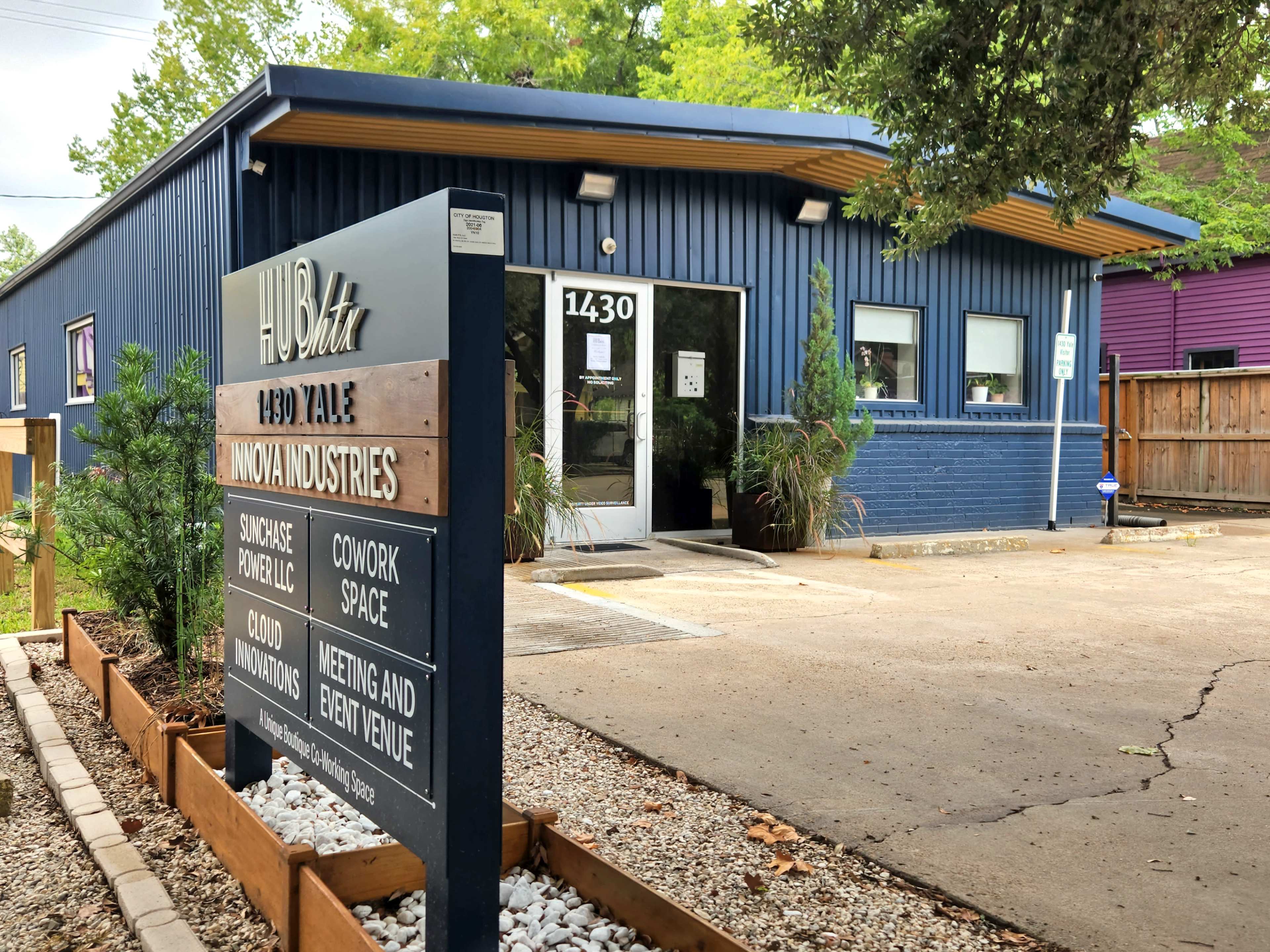 The image shows a blue commercial building with a sign for "HUB 1430" and "Innovate Industries," featuring a parking lot and landscaping with gravel and plants.