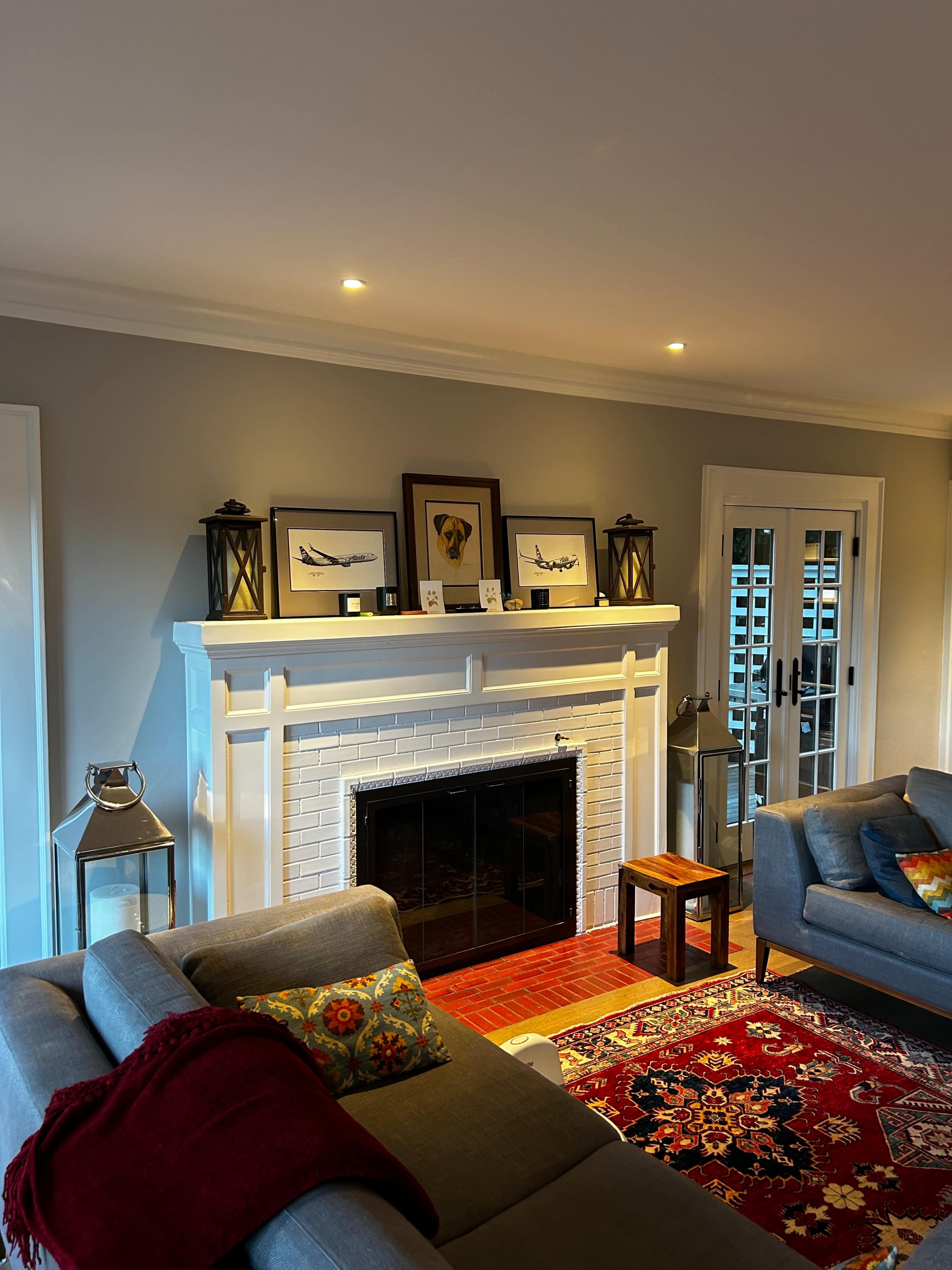 A cozy living room with a white brick fireplace, framed artwork above it, and two gray sofas positioned around a colorful area rug.