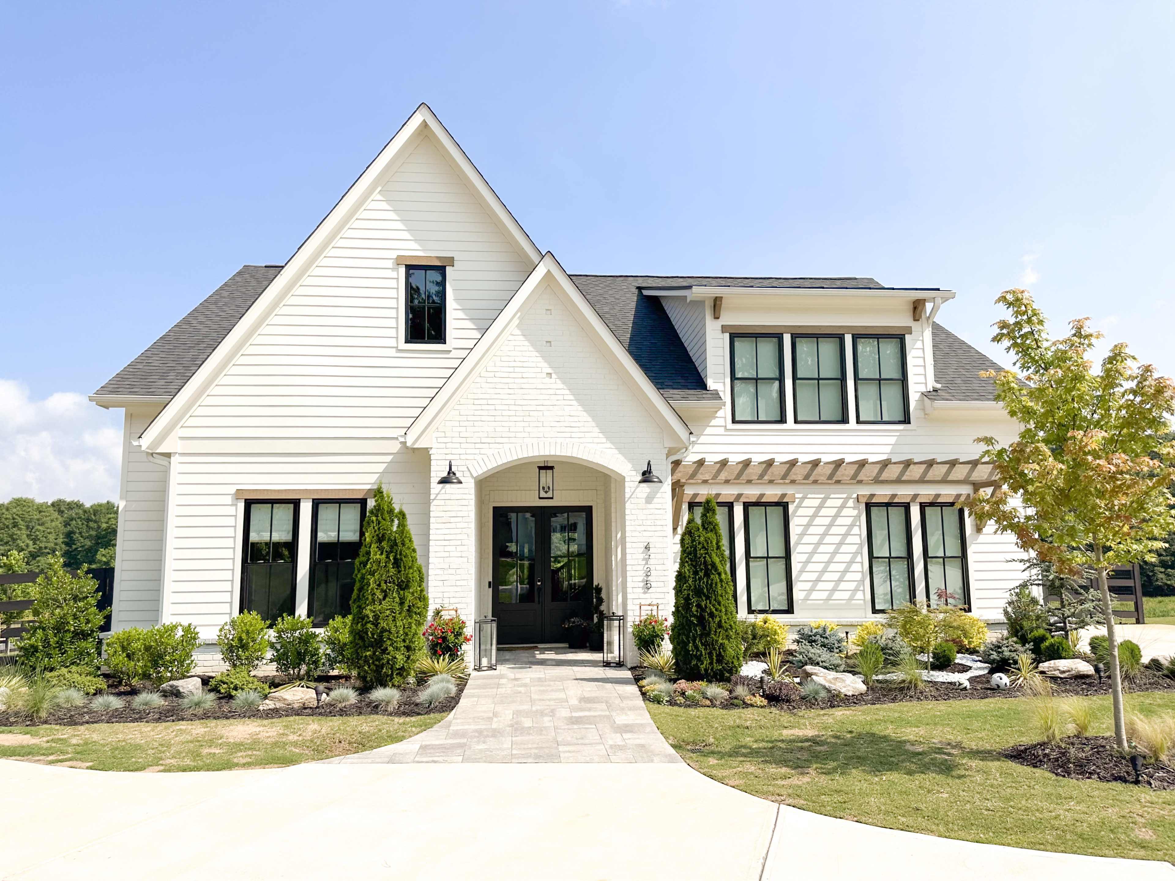 A two-story, modern-style house with white siding, black windows, and a landscaped front yard.