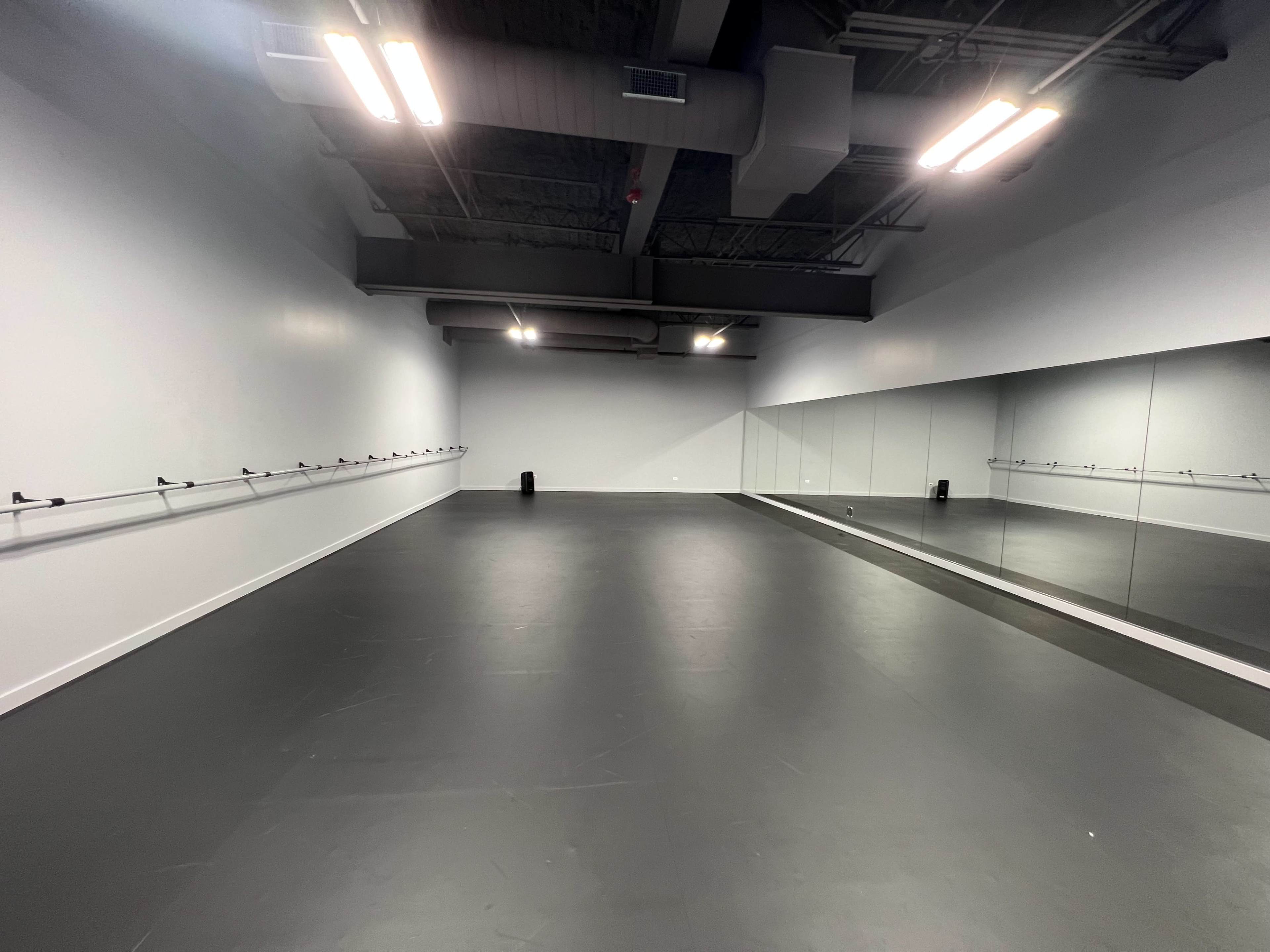 The image shows an empty dance studio with a mirrored wall and barre along one side.
