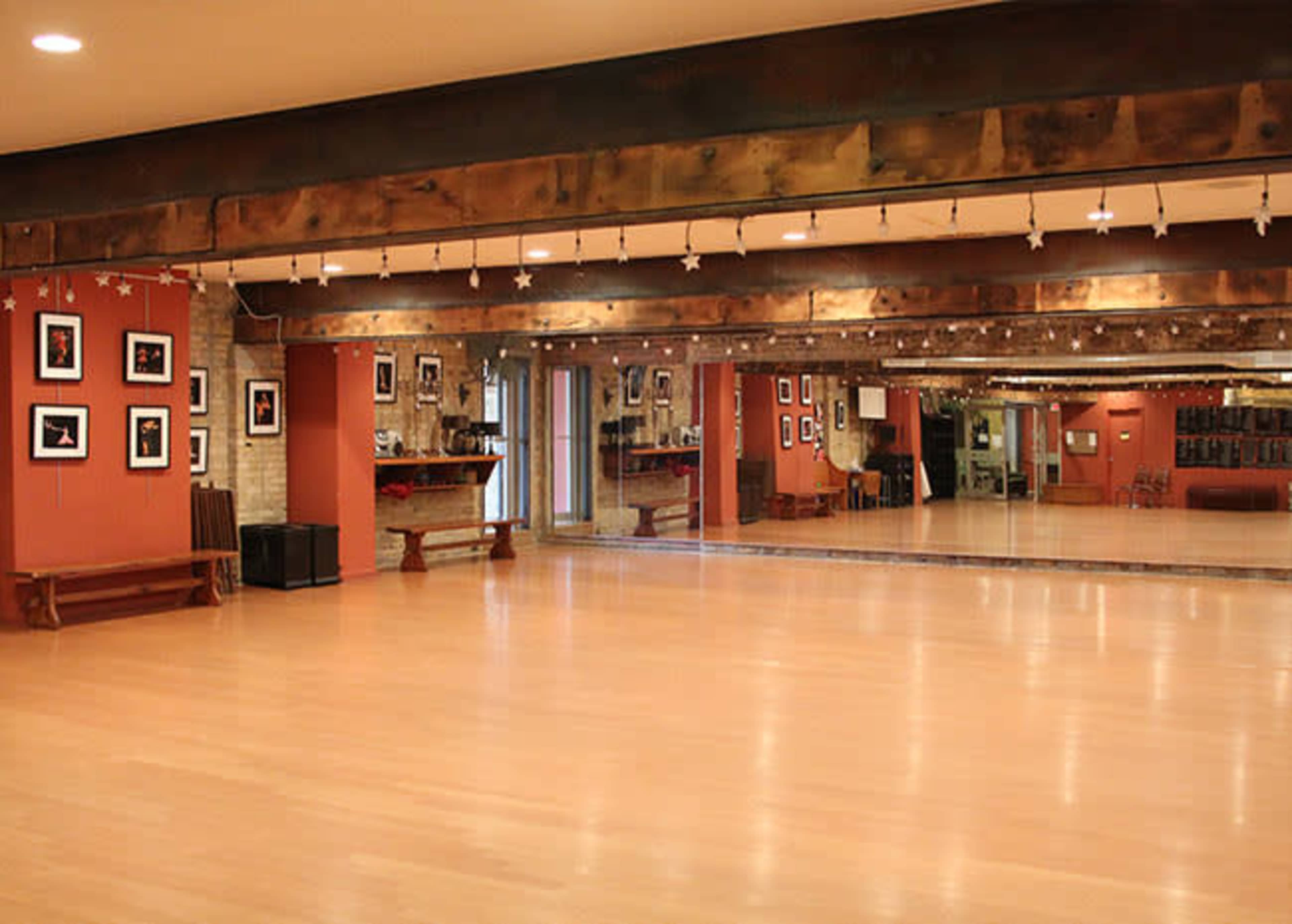 A spacious dance studio with wooden beams, mirrored walls, and framed photographs lining the reddish walls.