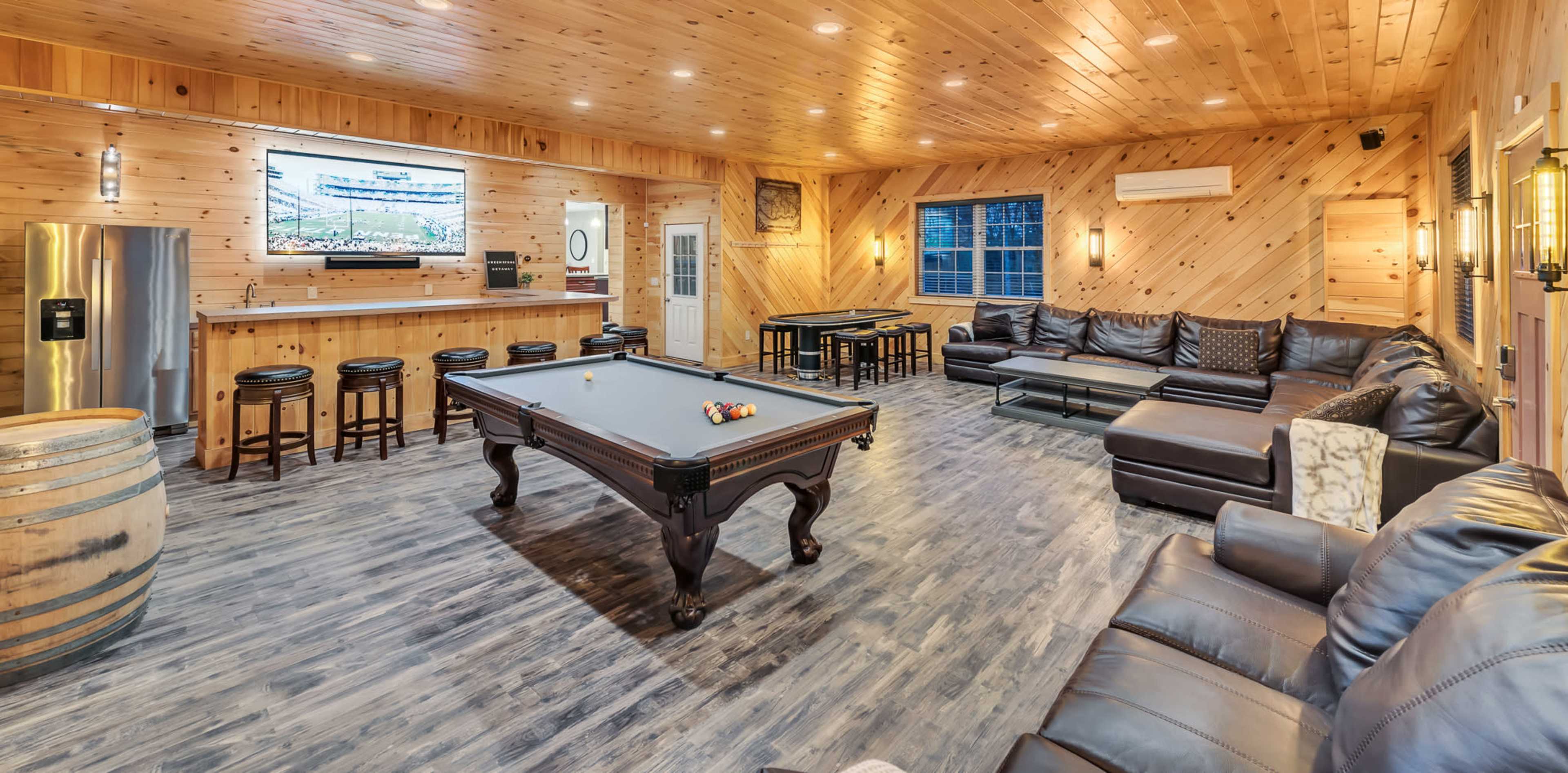 The room features a wooden-paneled game area with a pool table, seating arrangements, a large TV, and a bar counter.