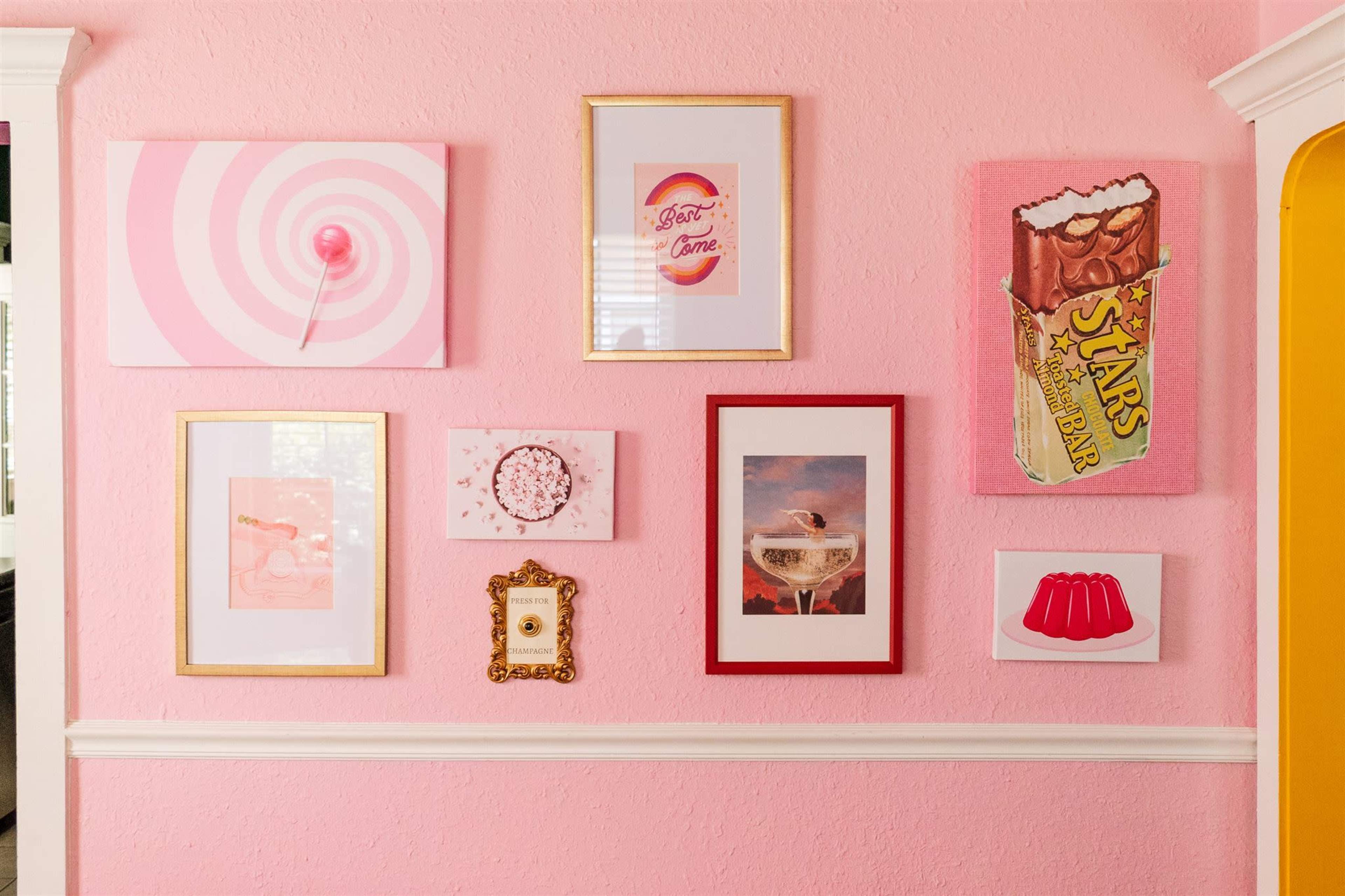 A pink wall displays a variety of framed artworks, including a lollipop, a cocktail, and a candy bar illustration.