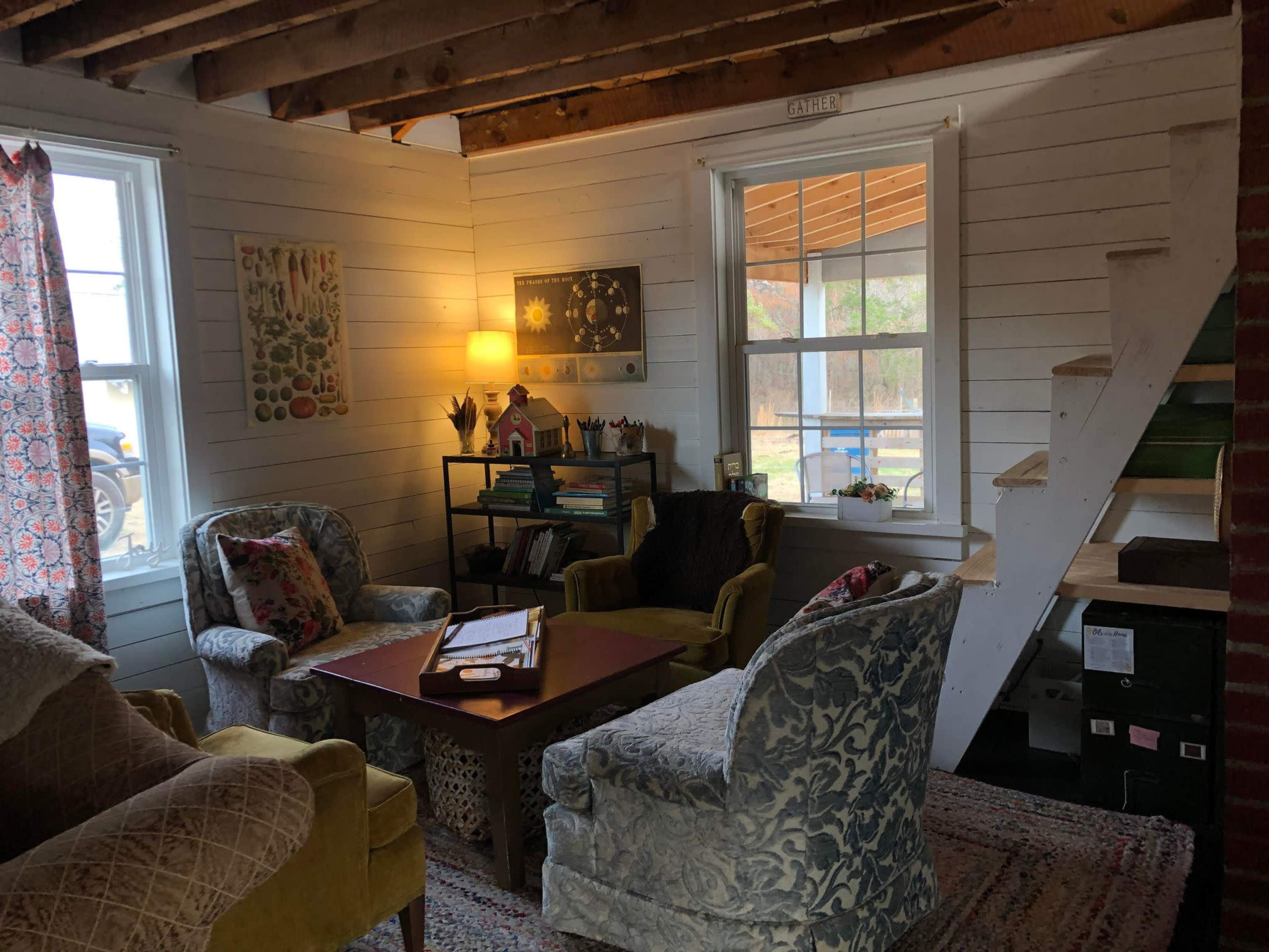 A cozy living room with two patterned chairs, a small table in the center, and a staircase leading to an upper level.