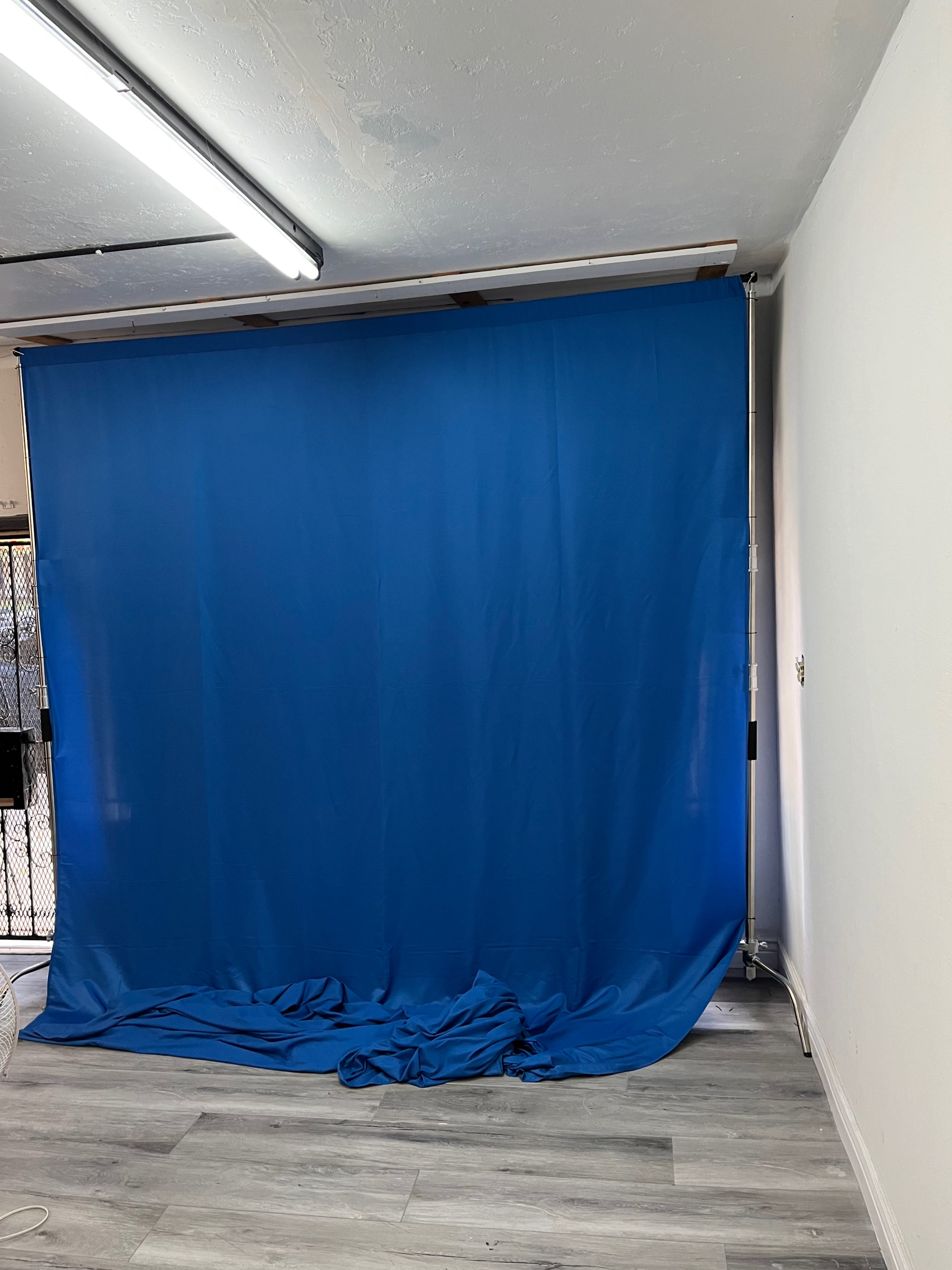 The image shows a blue backdrop draped on the floor in a well-lit room with gray flooring and white walls.