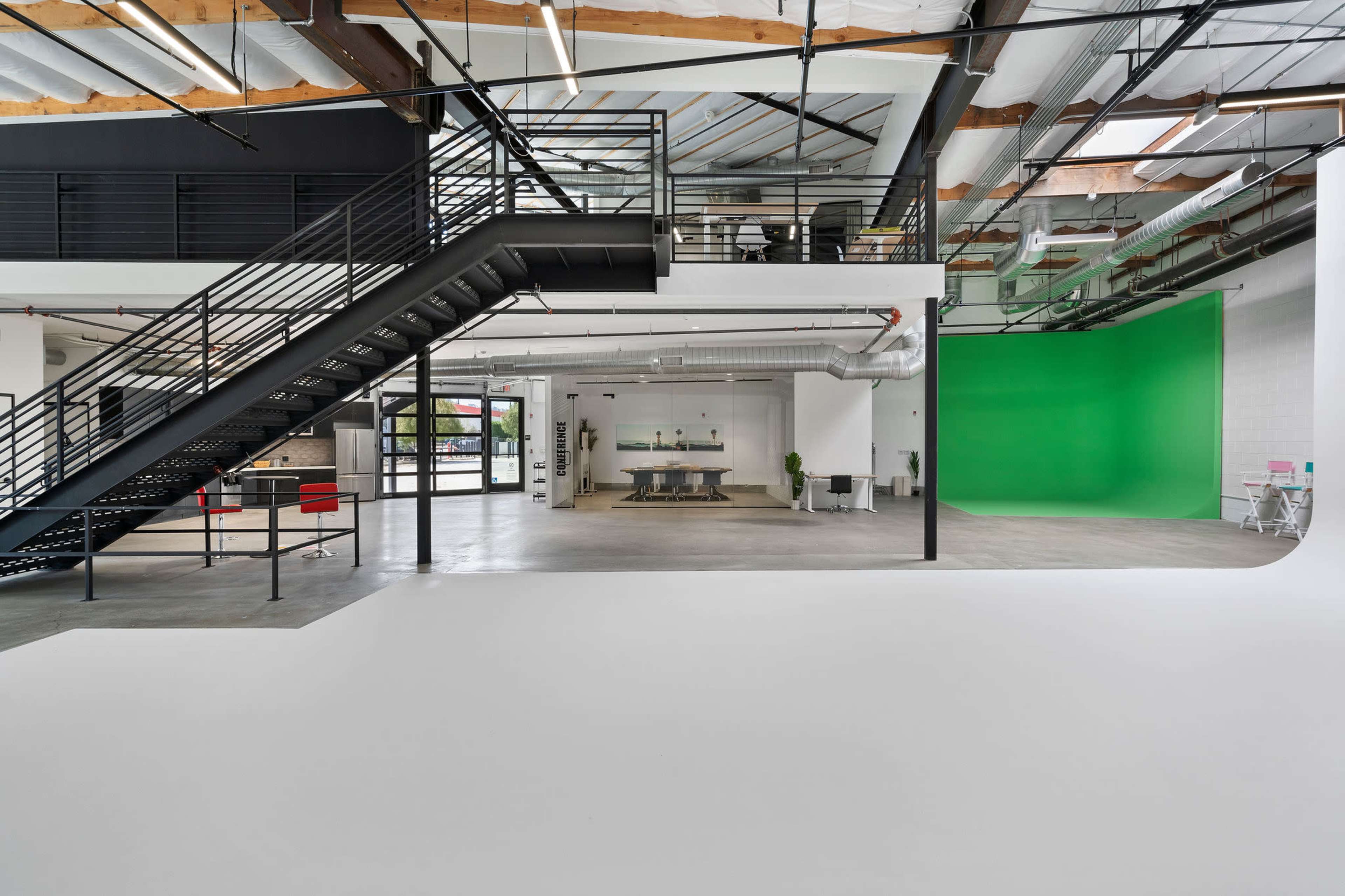 A spacious interior featuring a staircase, an open area with a kitchen table, and a green screen backdrop on the far wall.