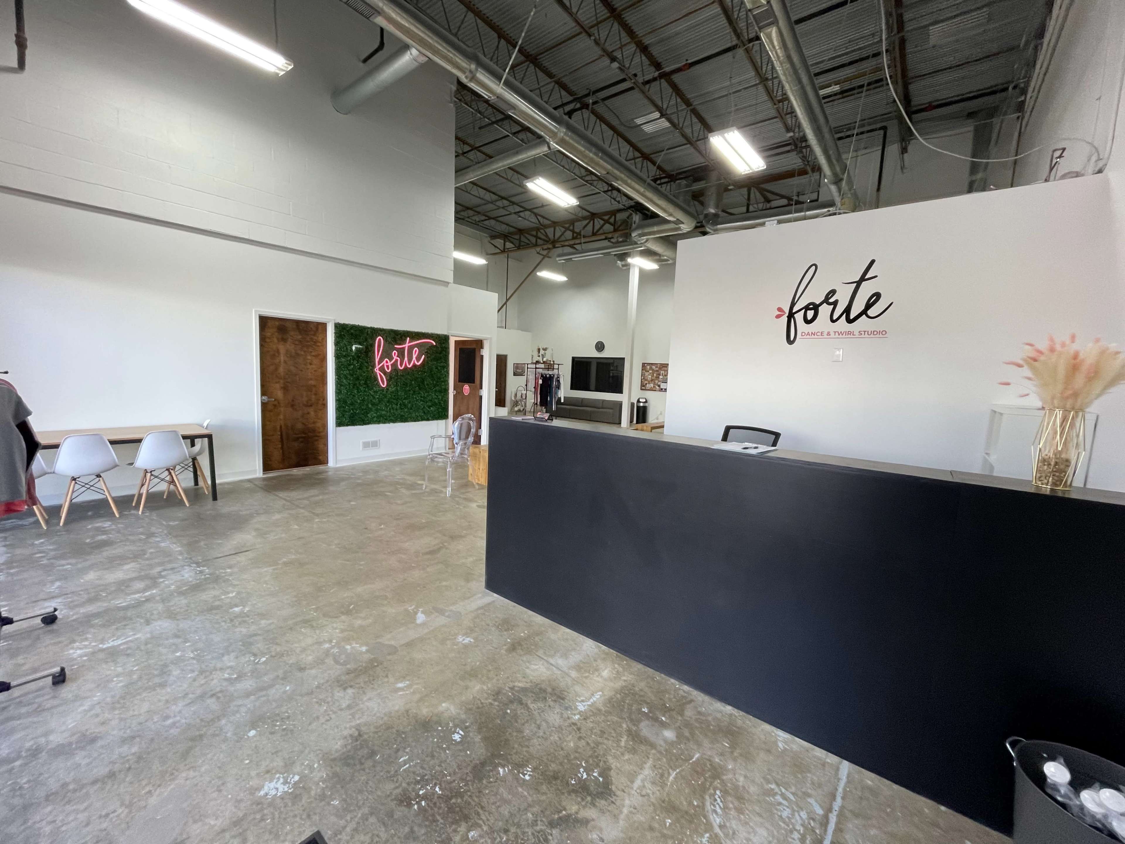 A modern interior of a studio or office space with a reception area featuring a black counter and decorative wall signage, alongside a seating area with white chairs and a green plant wall.