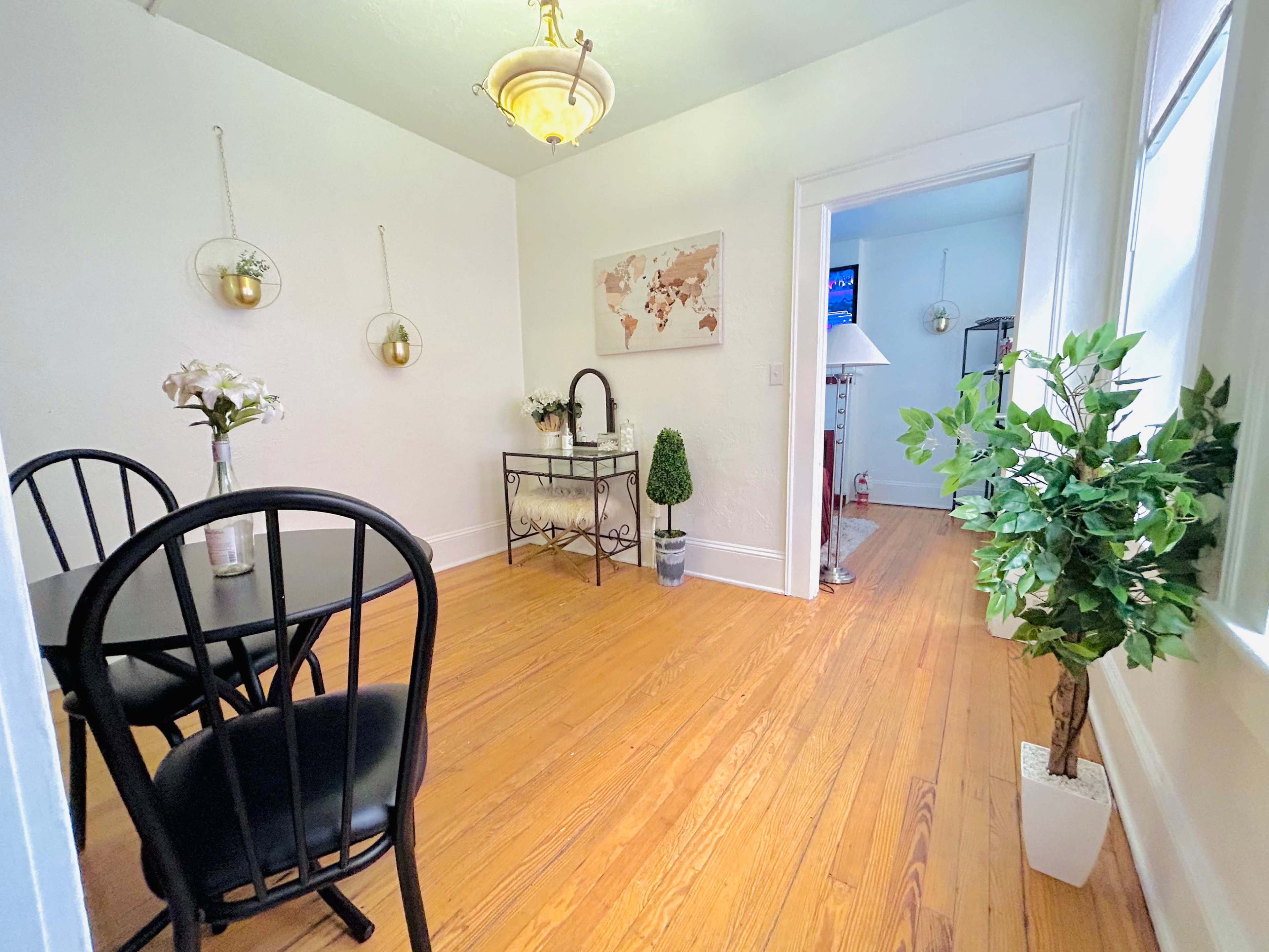 A bright, neatly arranged dining space featuring a black table and chairs, a decorative map on the wall, and potted plants.