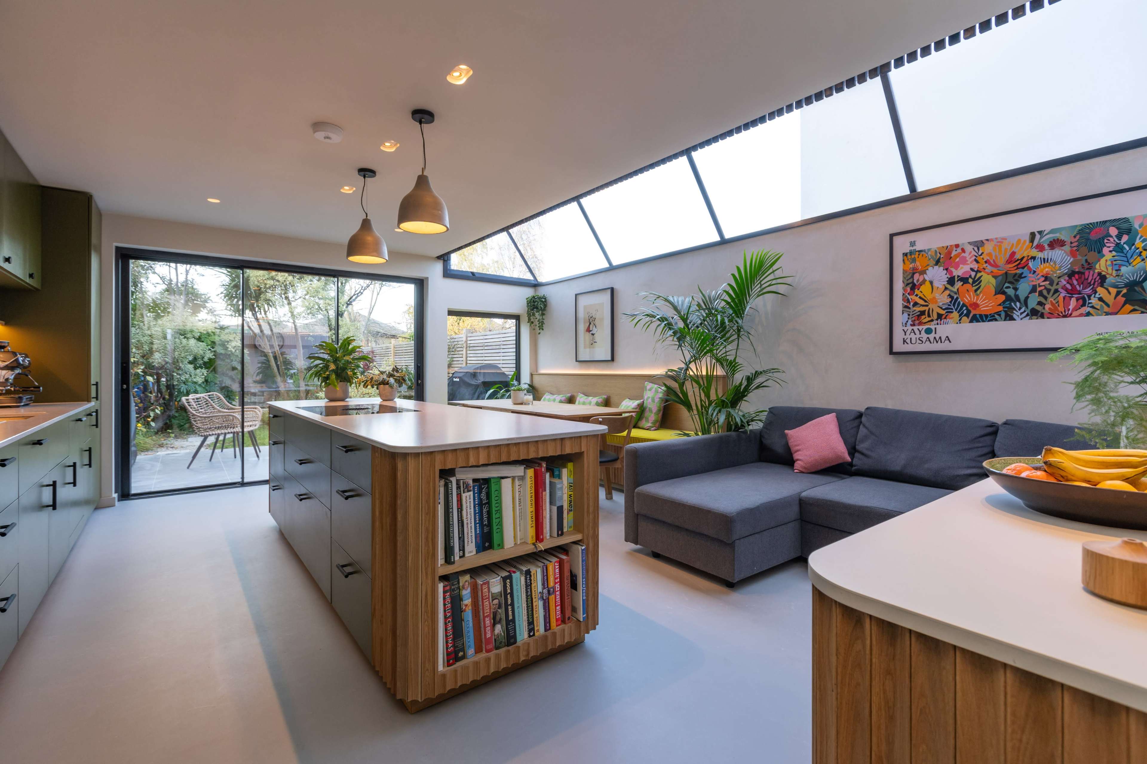 The image shows a modern kitchen and living area with a large island, a sectional sofa, and large glass doors leading to an outdoor space.