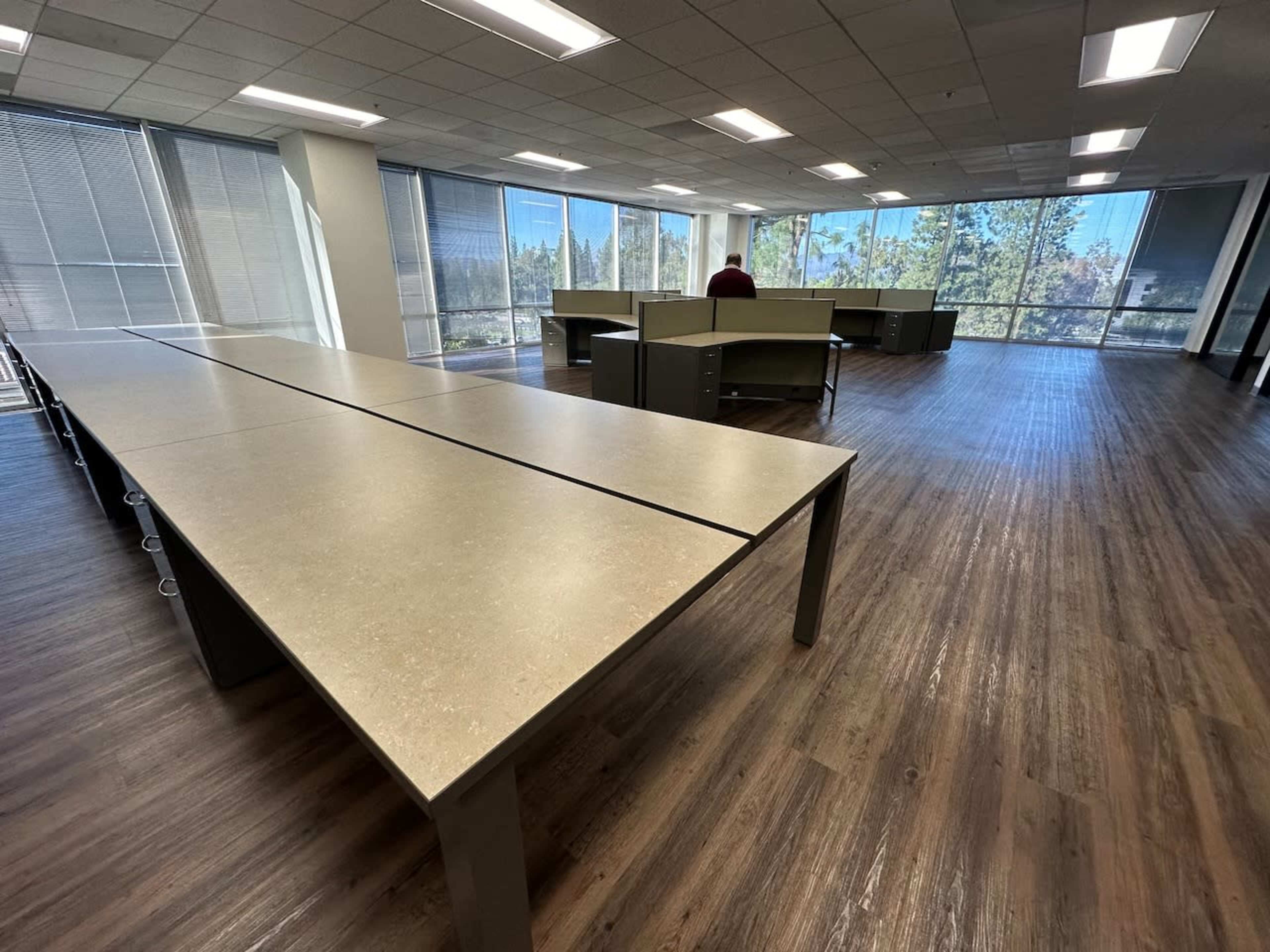 A spacious, modern office interior with large tables arranged in an open layout and multiple windows allowing natural light to enter.