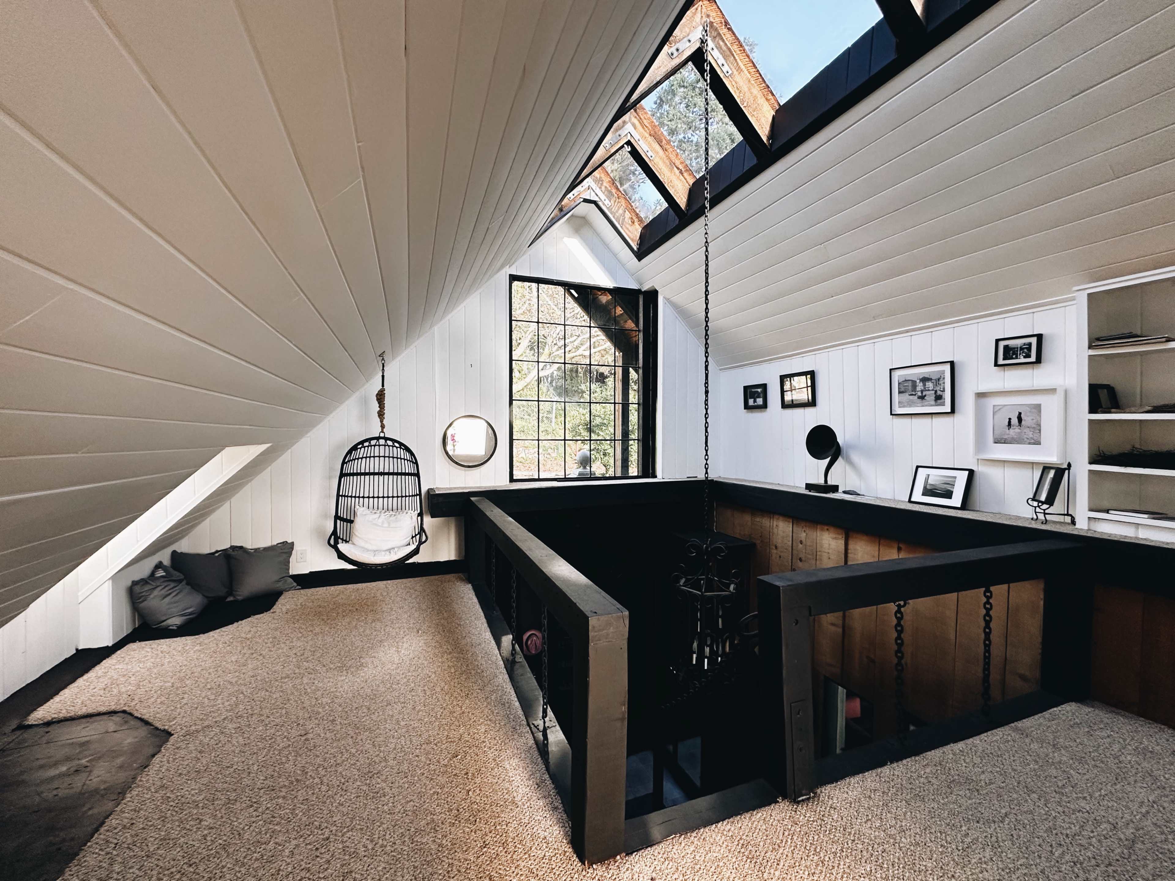 A modern attic space with sloped ceilings, a hanging chair, and large windows providing natural light.