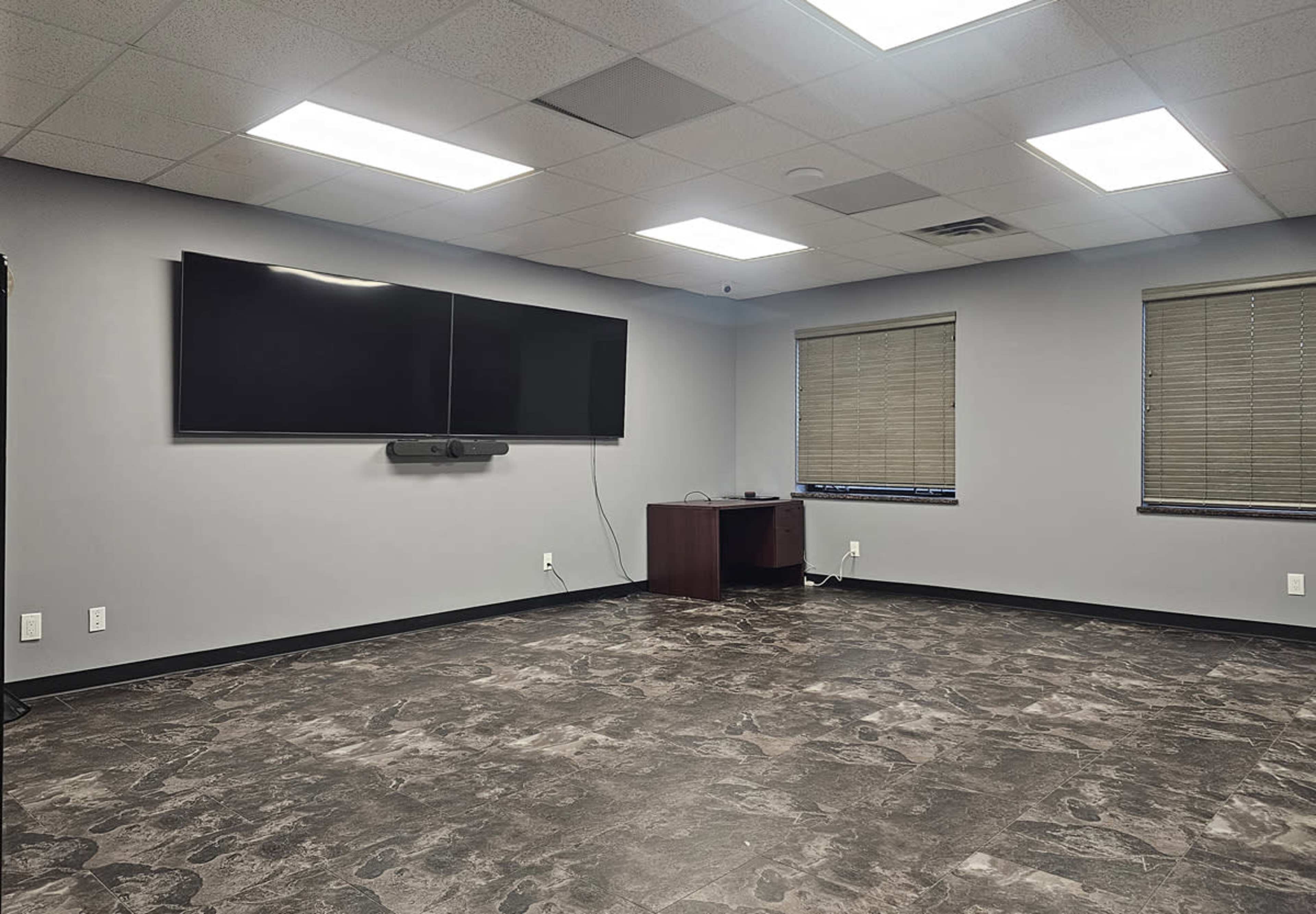 A modern conference room with a large flat-screen TV mounted on the wall and minimal furniture.