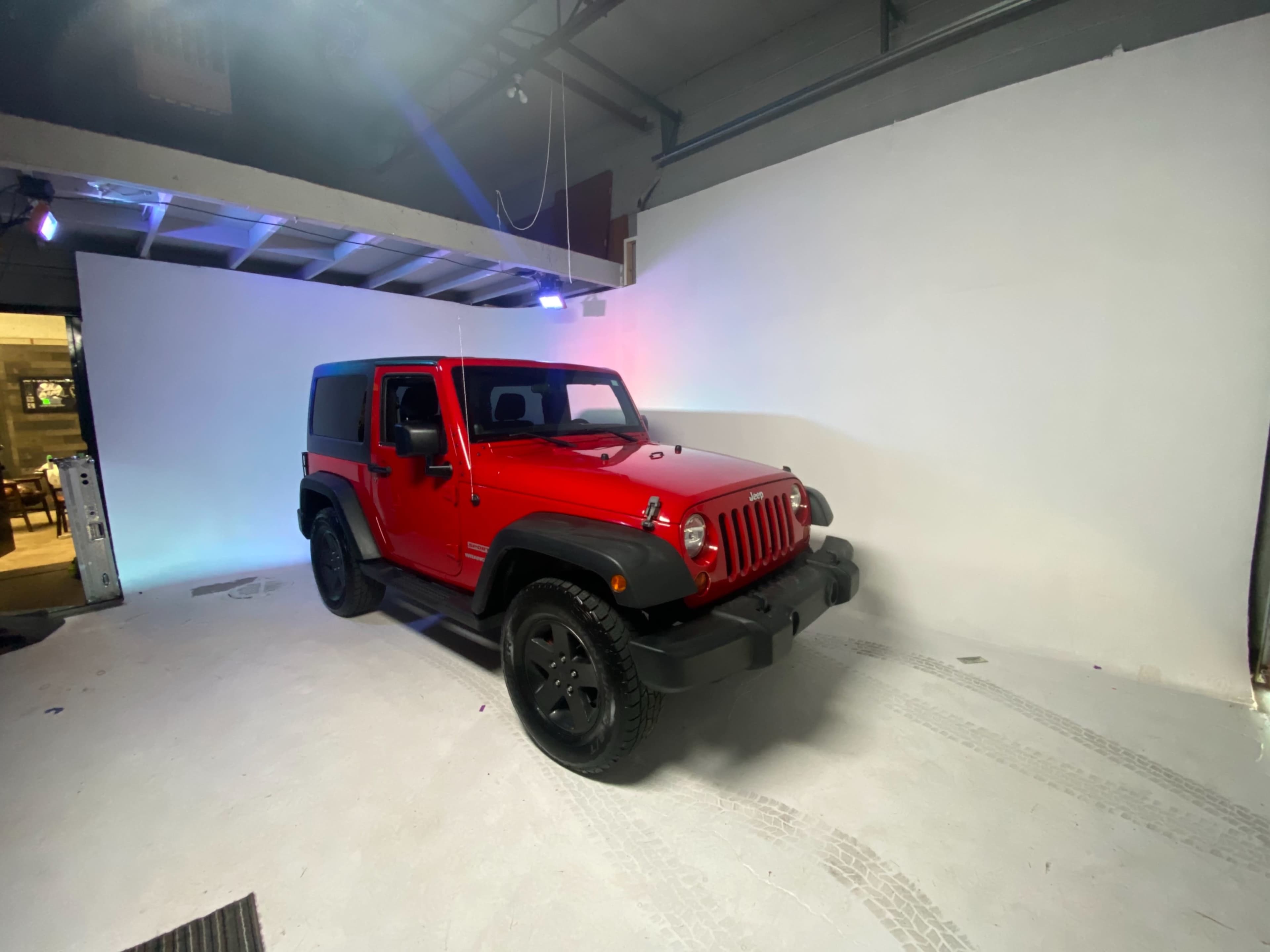 A red Jeep Wrangler is parked in a photo studio with a plain white backdrop.