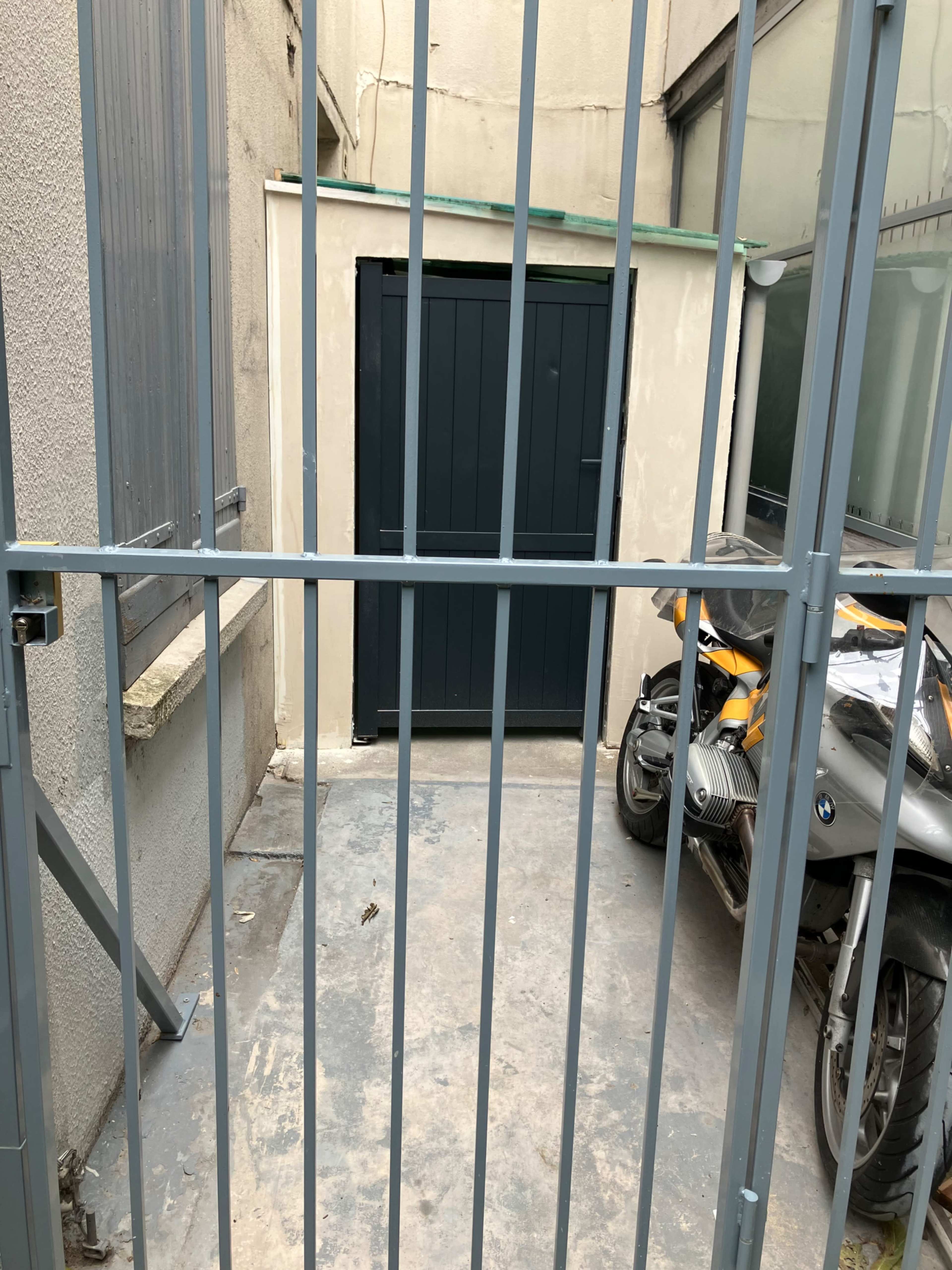 A gated entrance leads to a narrow alleyway with a closed dark door and a motorcycle parked beside it.