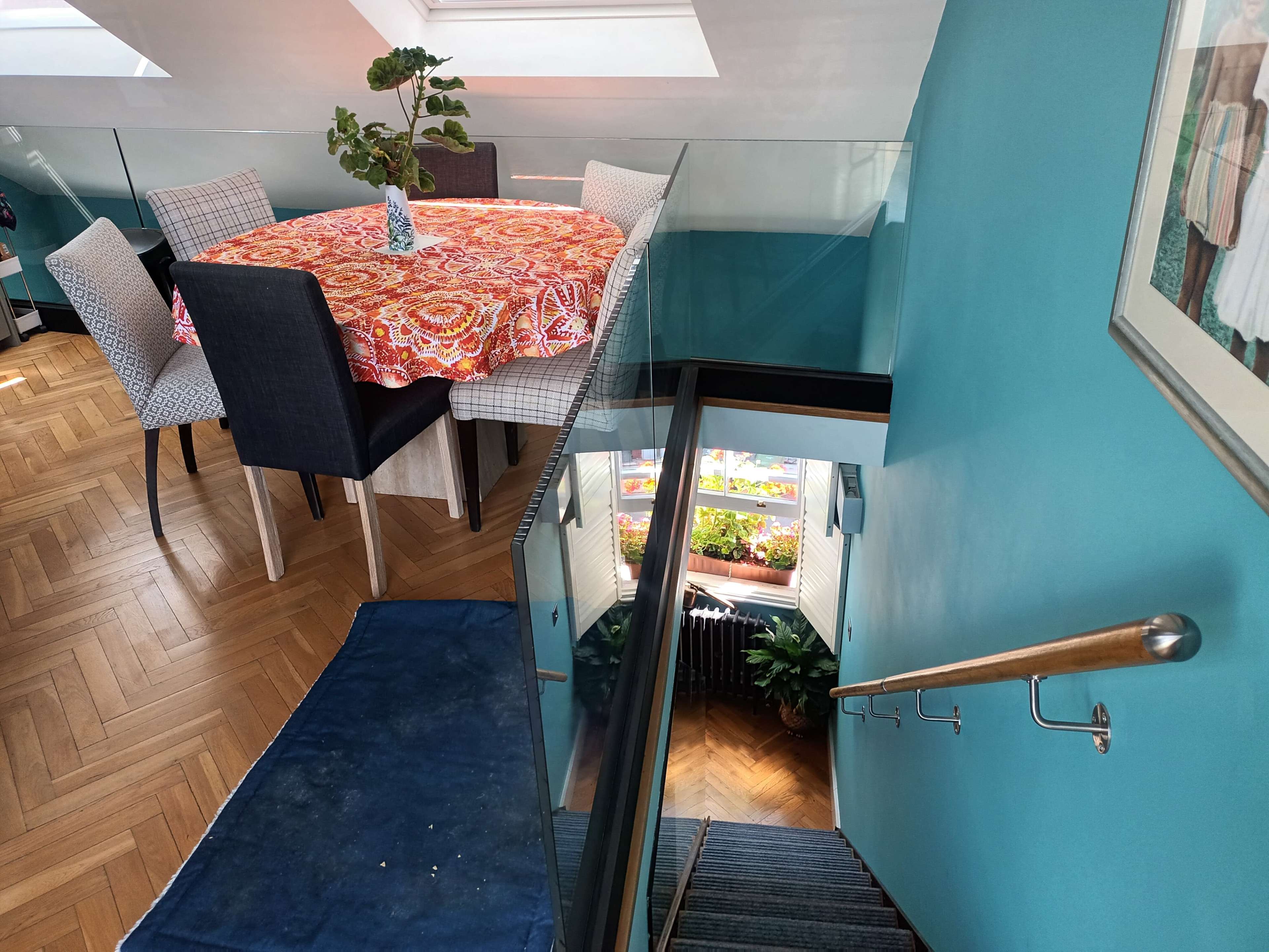A dining table with a colorful tablecloth is set near the top of a staircase leading down to a lower level adorned with plants.