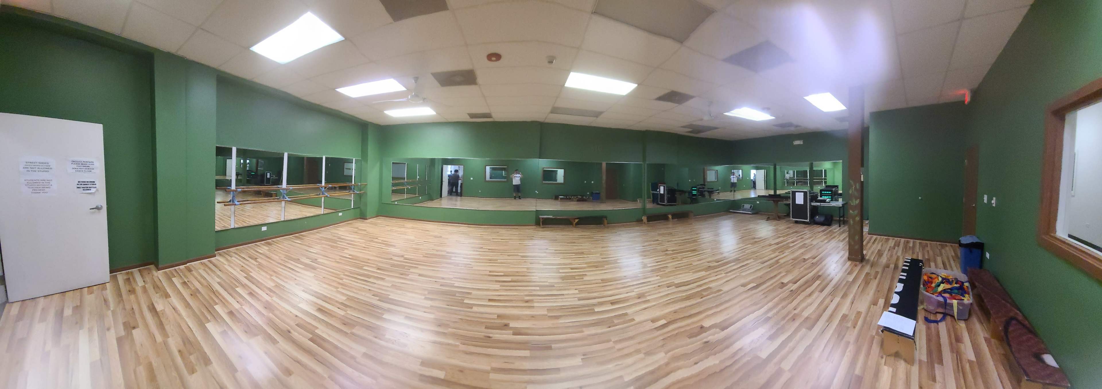 A spacious dance studio with green walls, wooden flooring, and large mirrors lining one side.