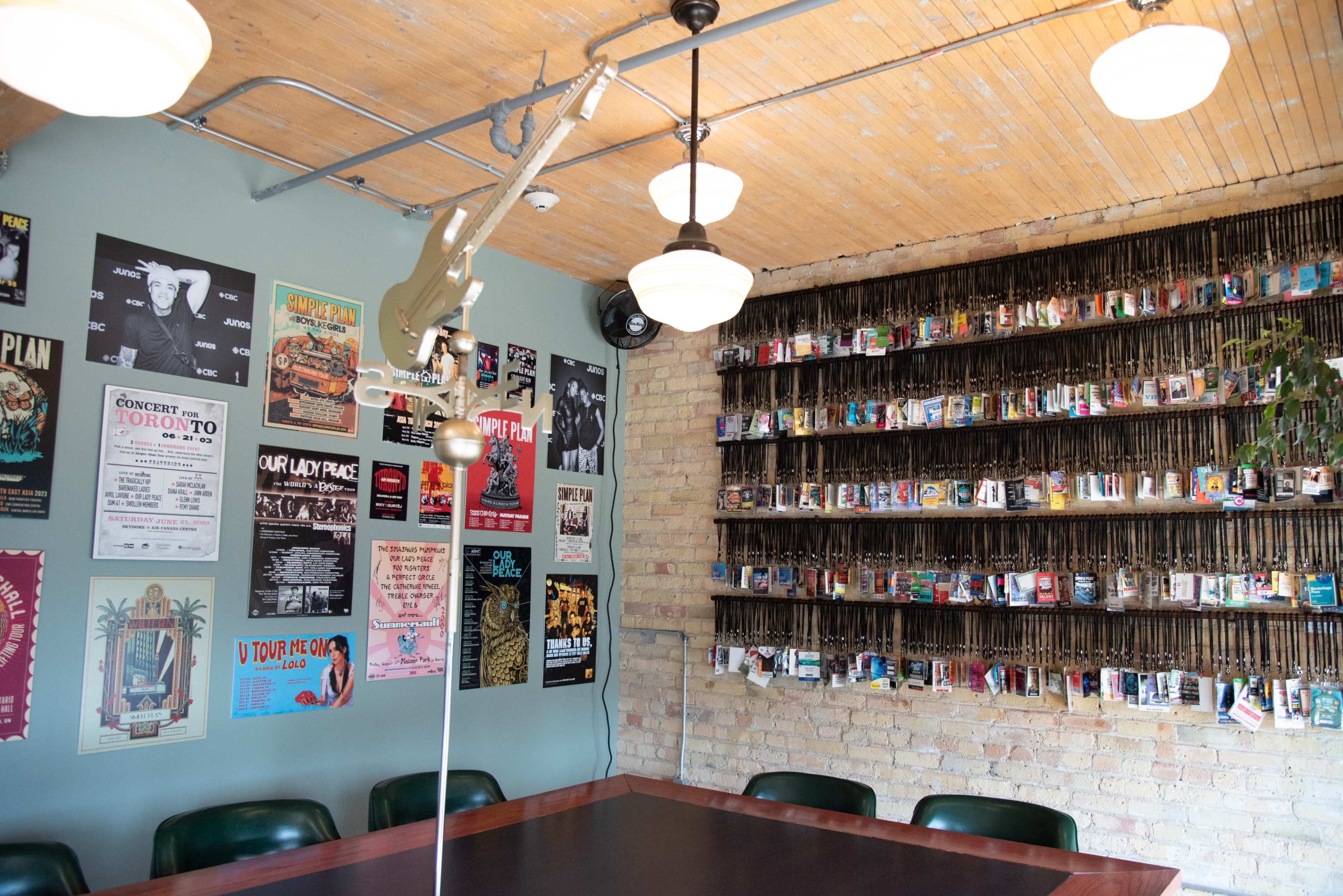 The image shows a modern cafe interior with a large wooden table, walls adorned with concert posters, and shelves lined with small objects.