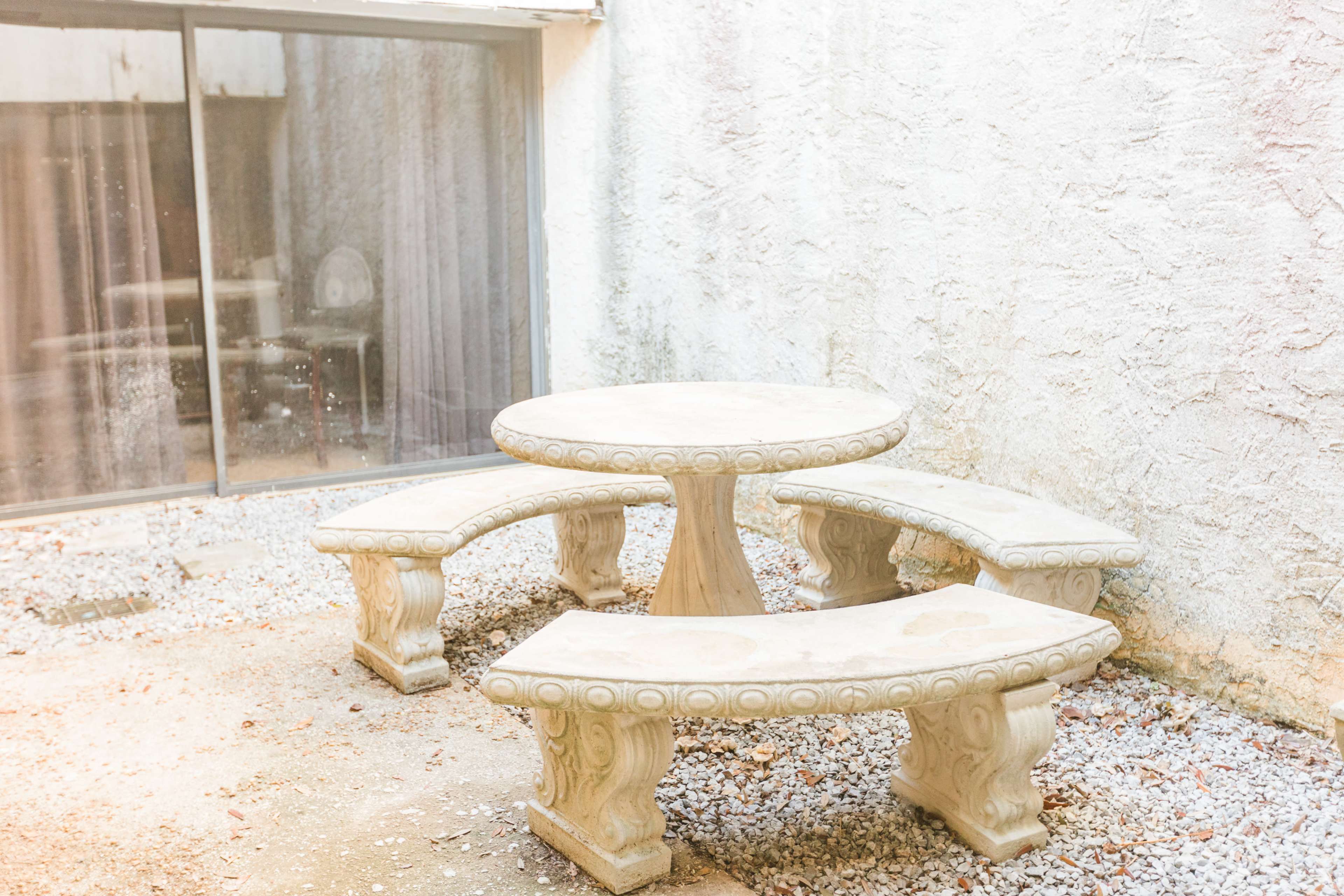 A circular stone table is surrounded by three matching curved benches in a gravel courtyard.