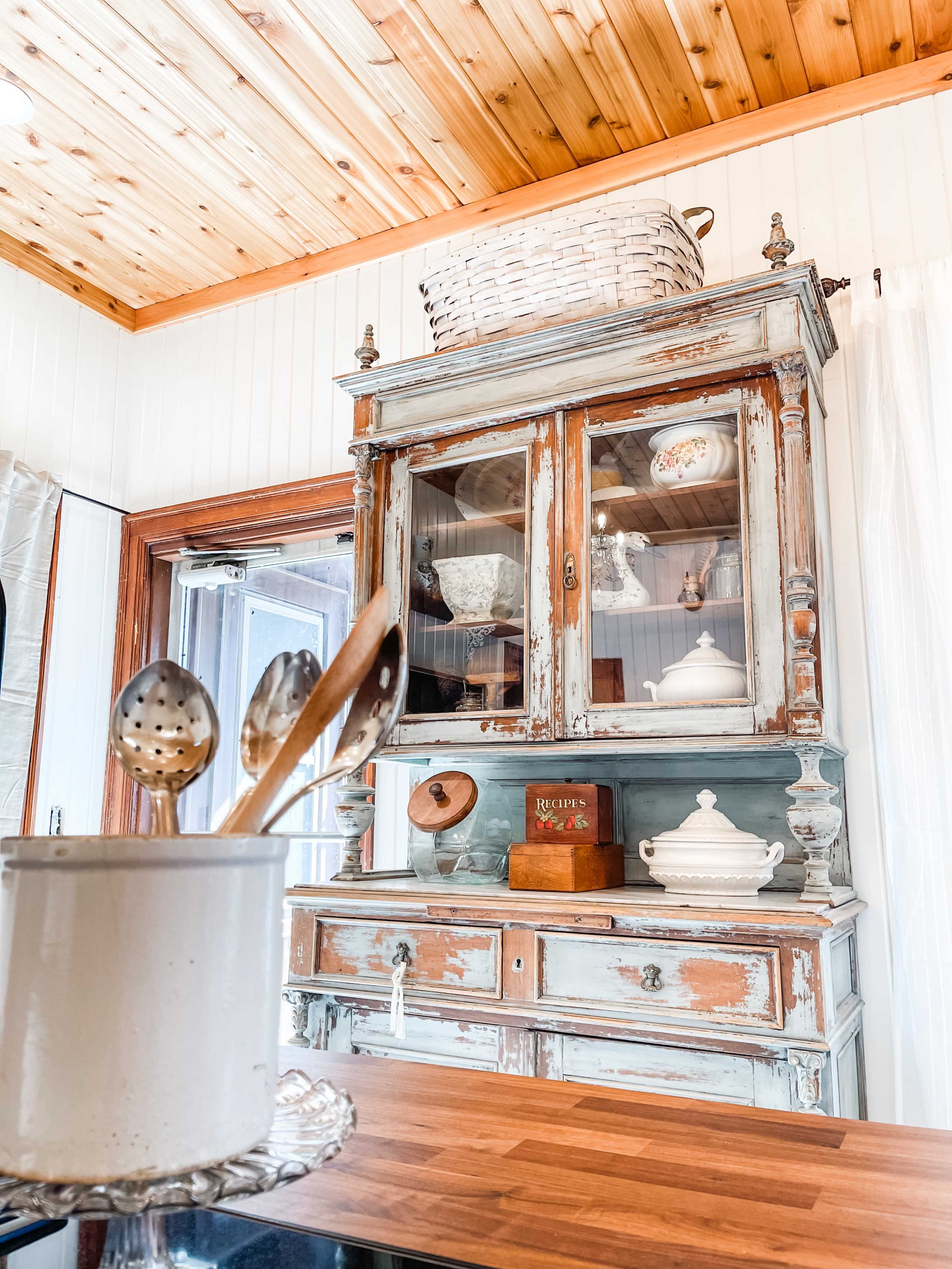 A rustic wooden kitchen with a vintage glass-front cabinet displaying dishware and decorative items.