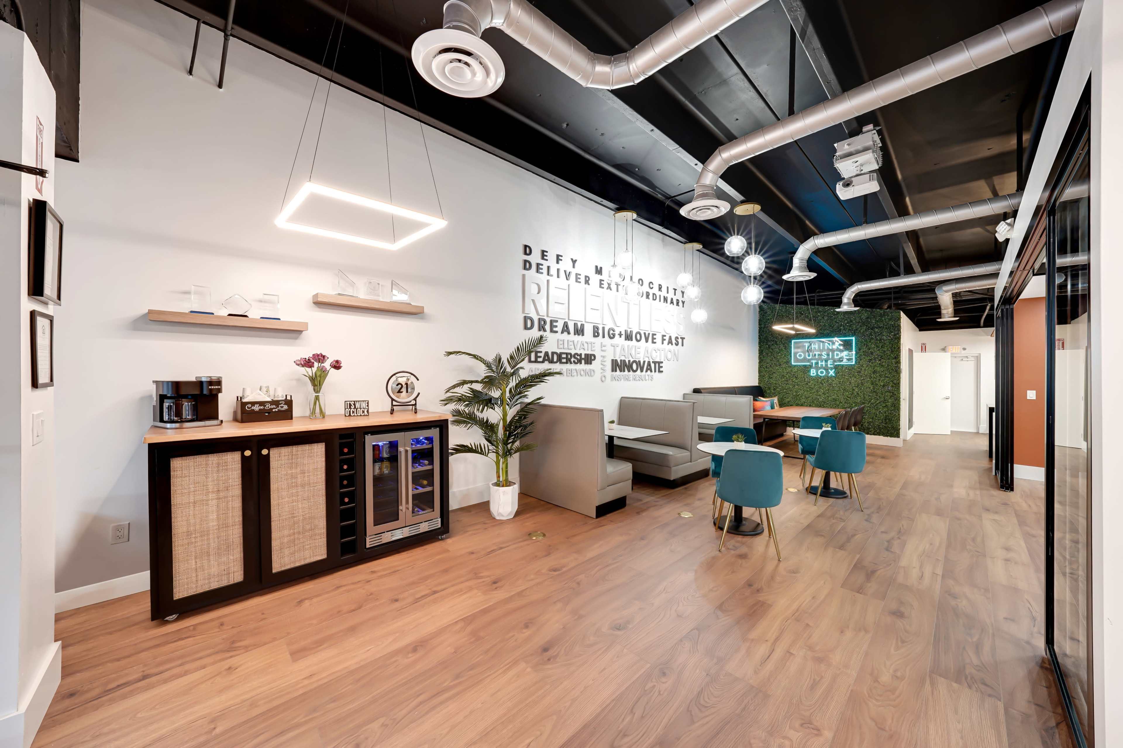A modern office break room featuring a kitchenette, seating area, and motivational wall decor.