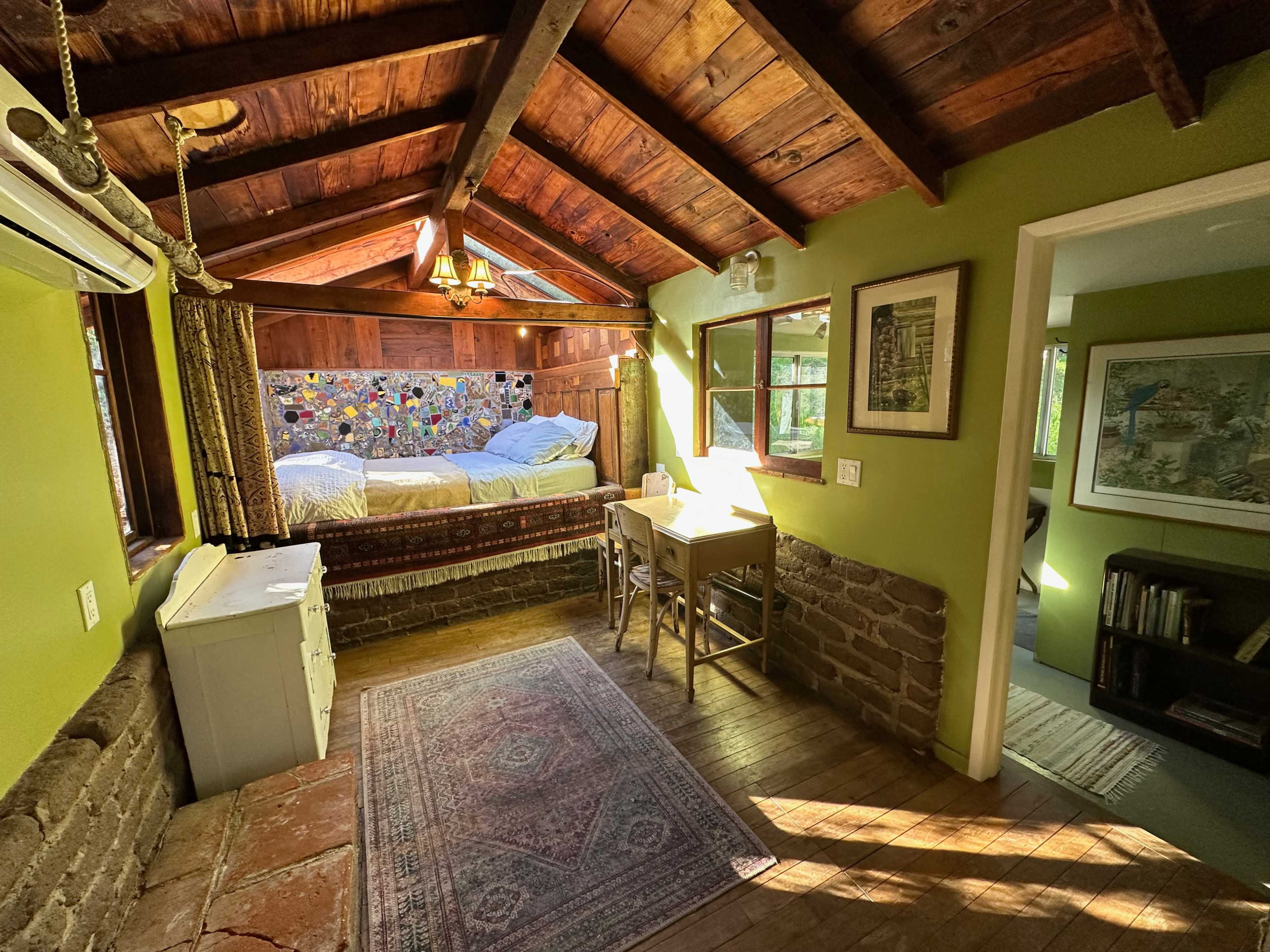 A cozy, rustic cabin interior featuring a bed with a colorful quilt, a small wooden table and chairs, and exposed wooden beams.