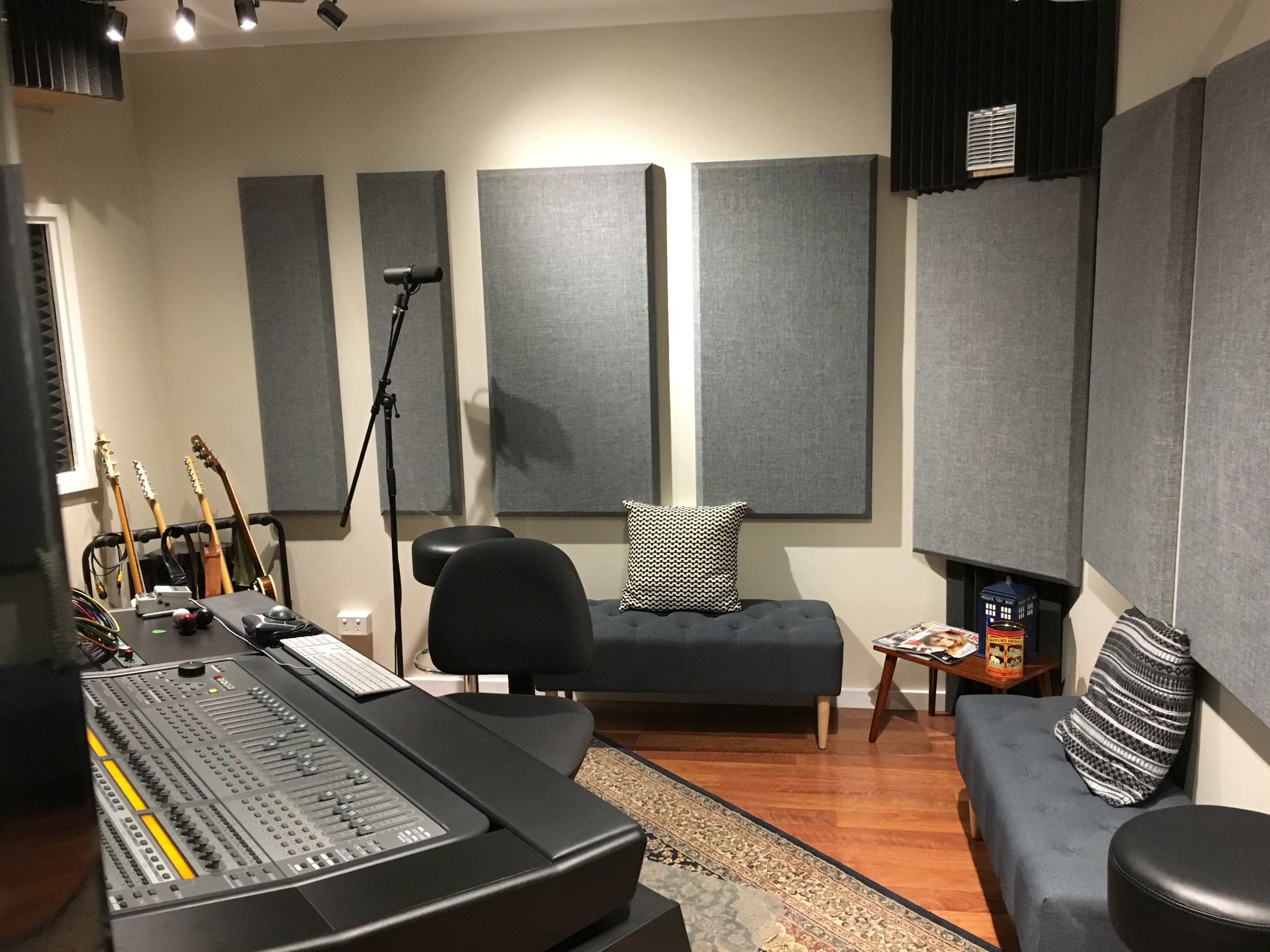 A recording studio with soundproof wall panels, a mixing console, and two couches along with guitars and magazines in the room.