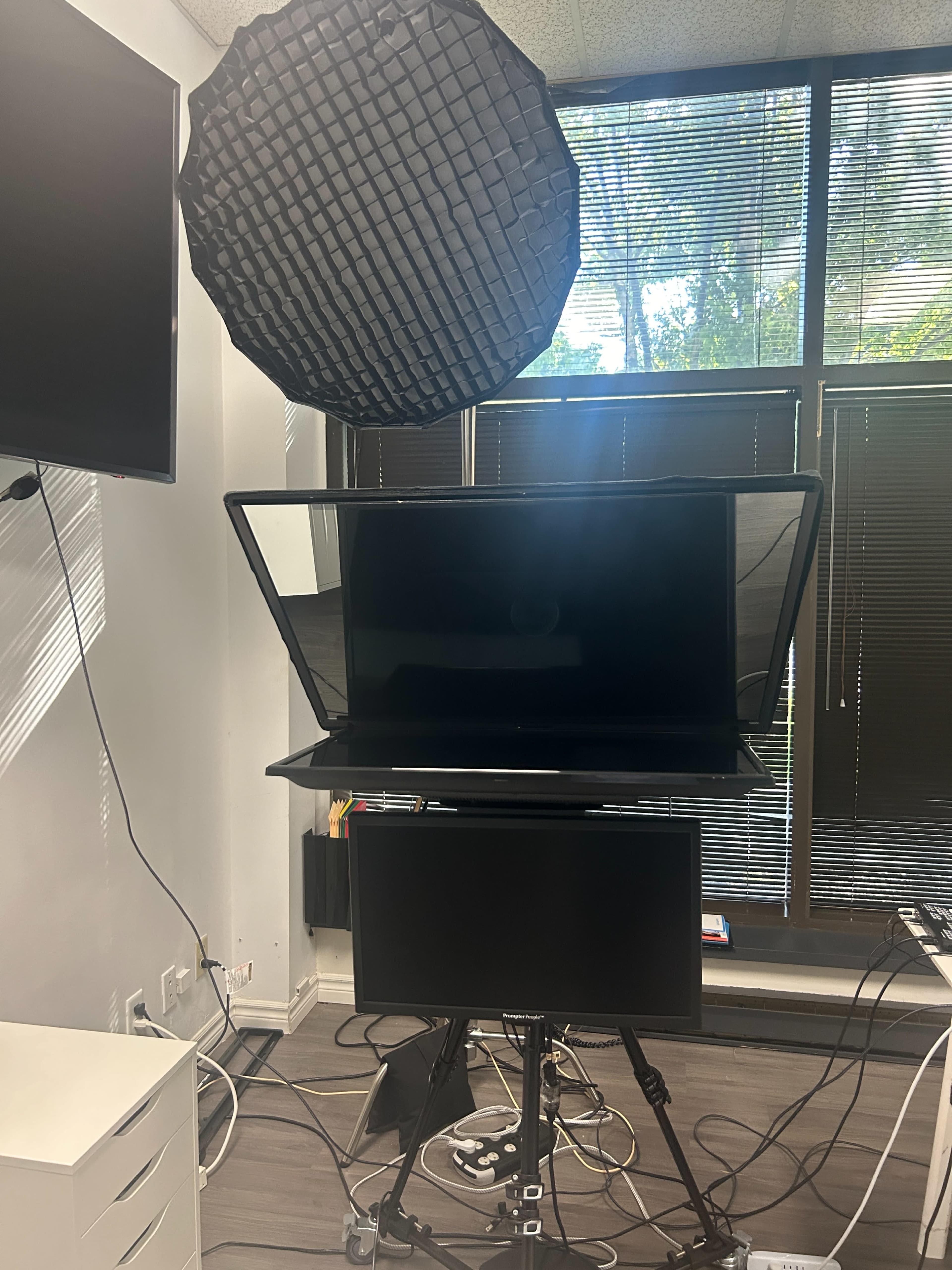 The image shows a video setup with a large softbox light above a dual monitor configuration in an office space.