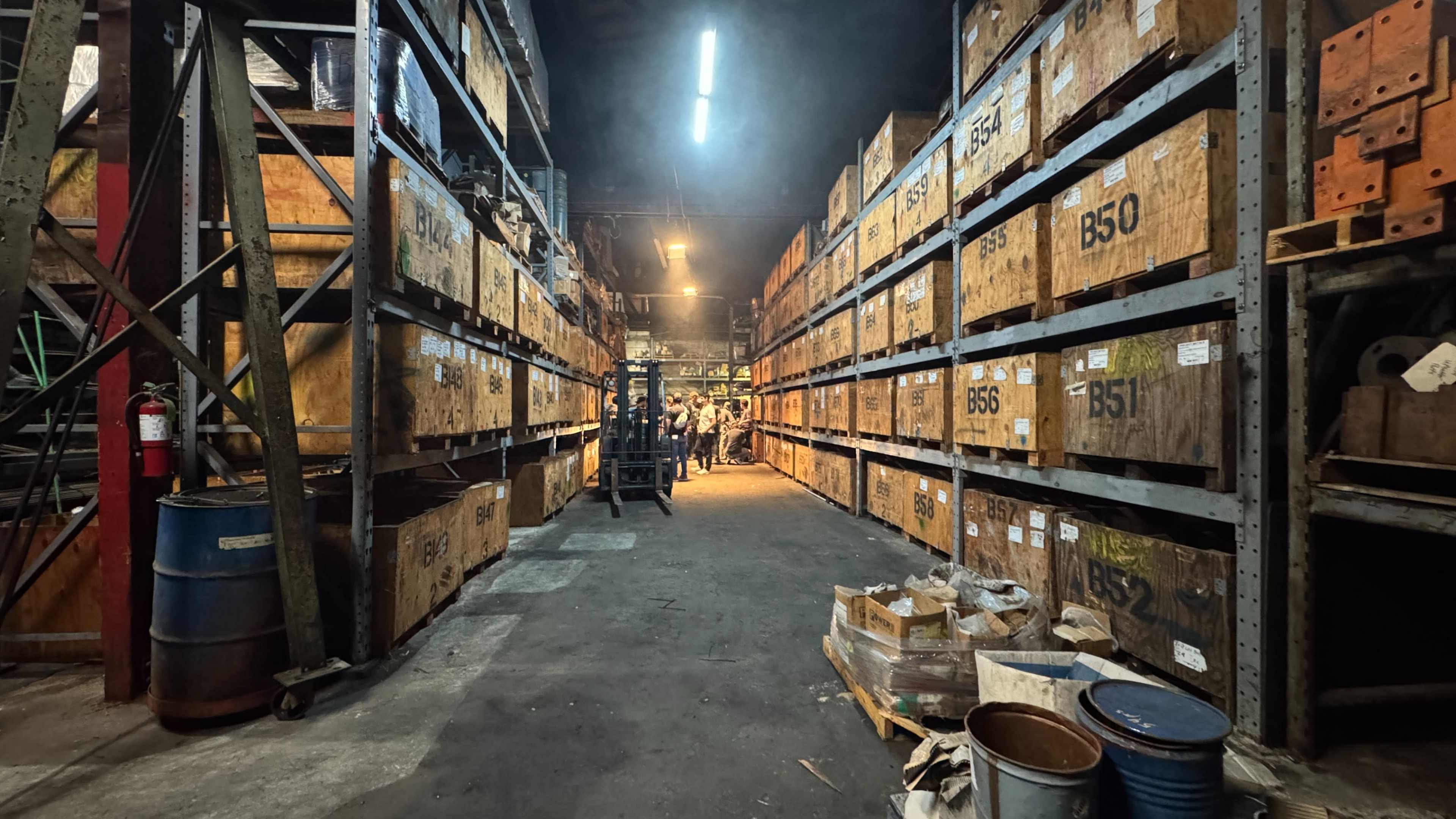 The image shows a warehouse aisle lined with tall wooden crates marked with numbers, illuminated by overhead lights.