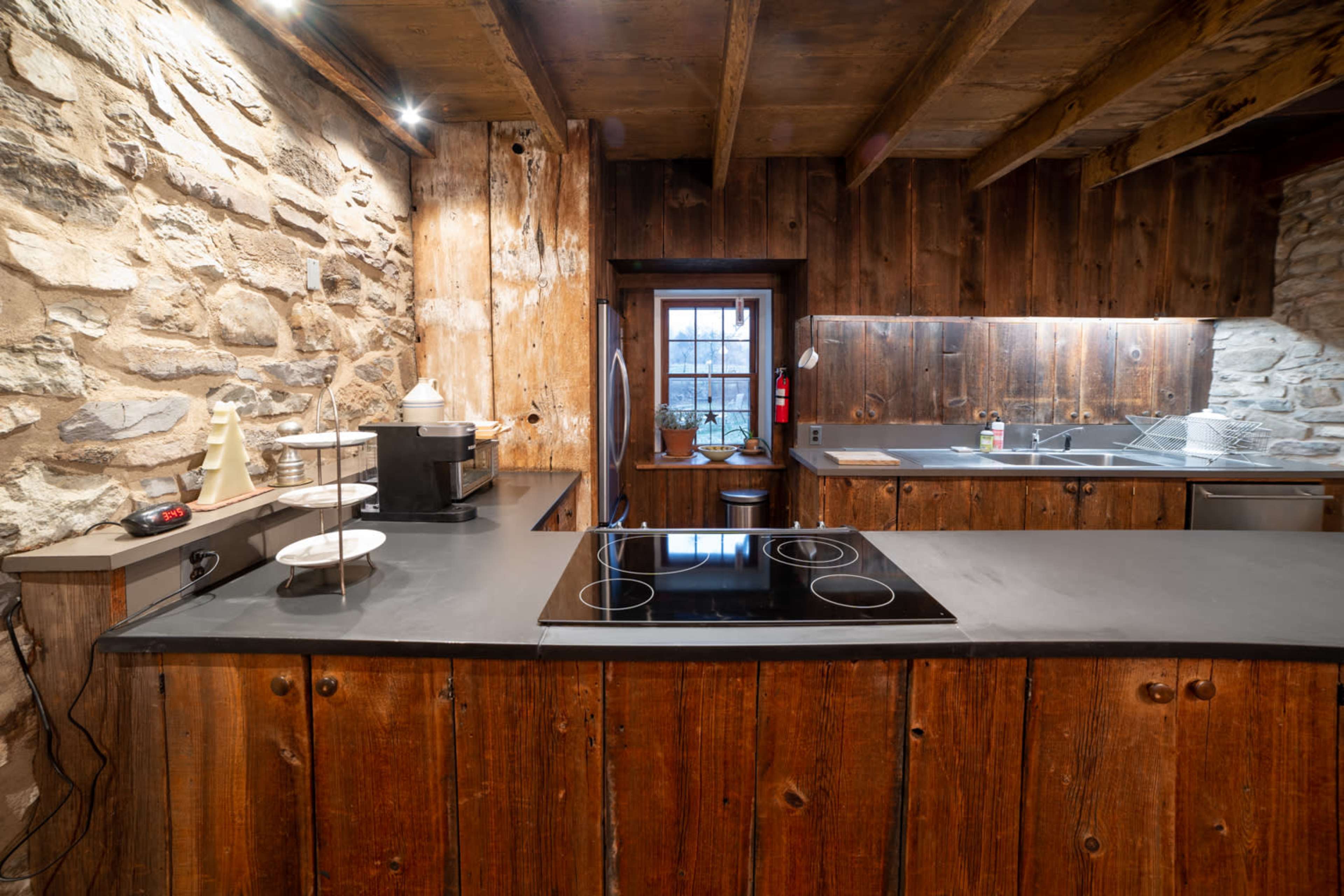 The image shows a rustic kitchen with stone and wooden walls, featuring a modern induction cooktop and an organized countertop.